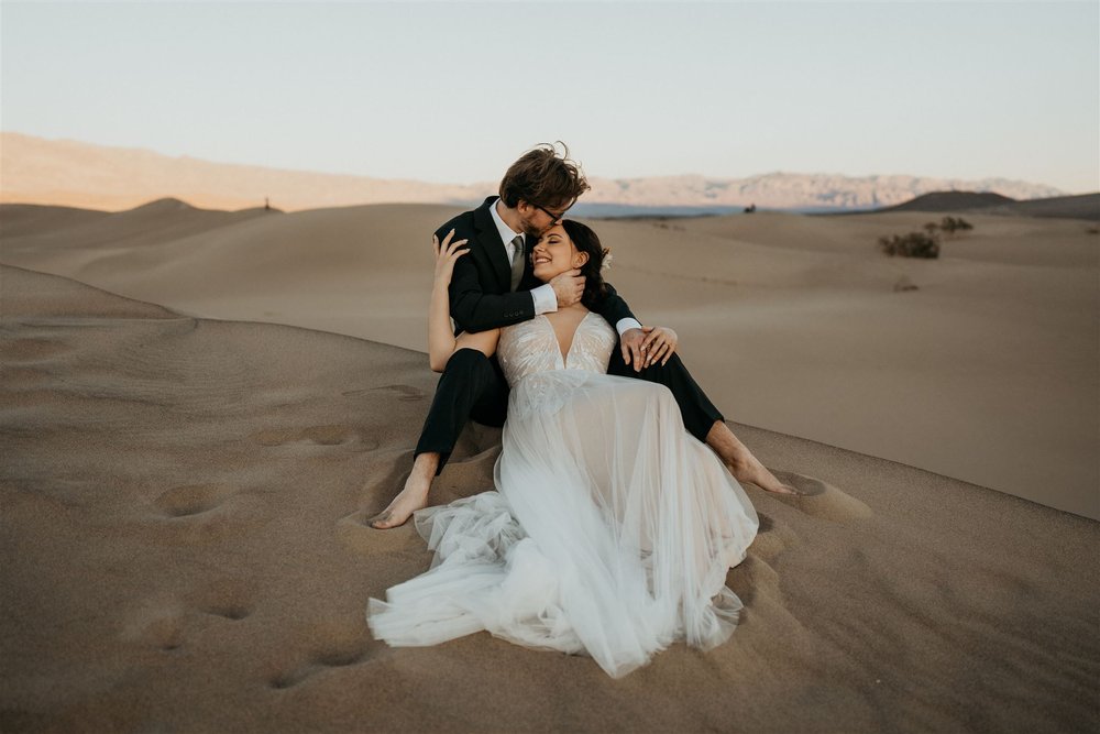 Bride and groom sit in sand dunes at Death Valley National Park for their California elopement photos
