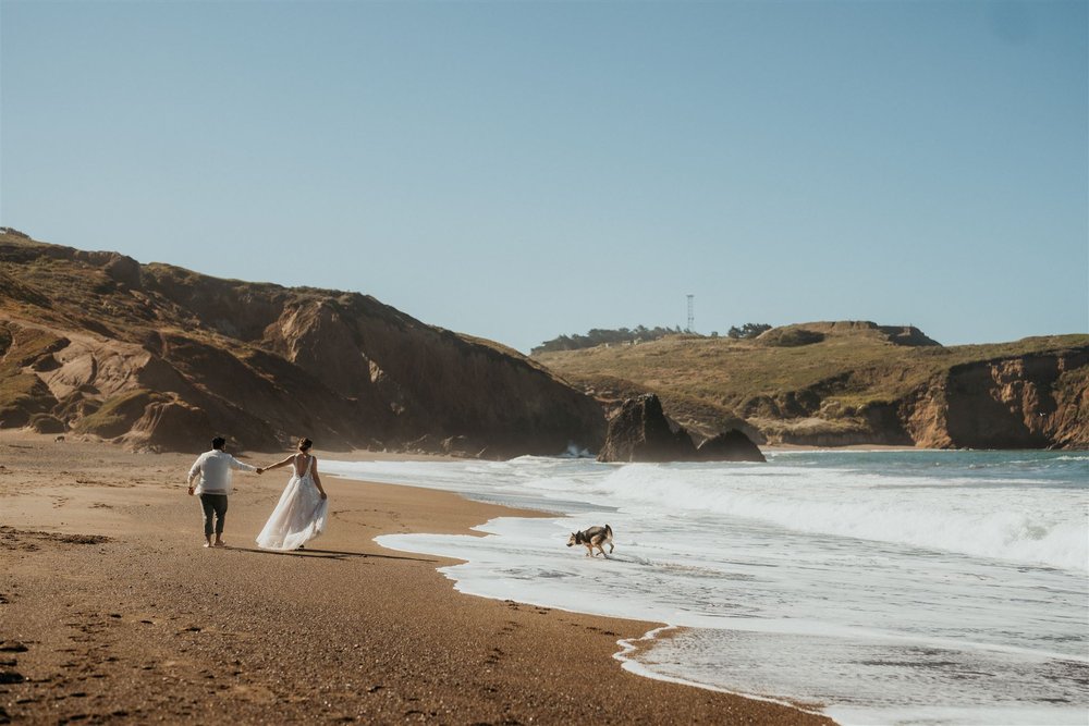 Bride and groom walk across the beach with their dog during their elopement in Marin Headlands