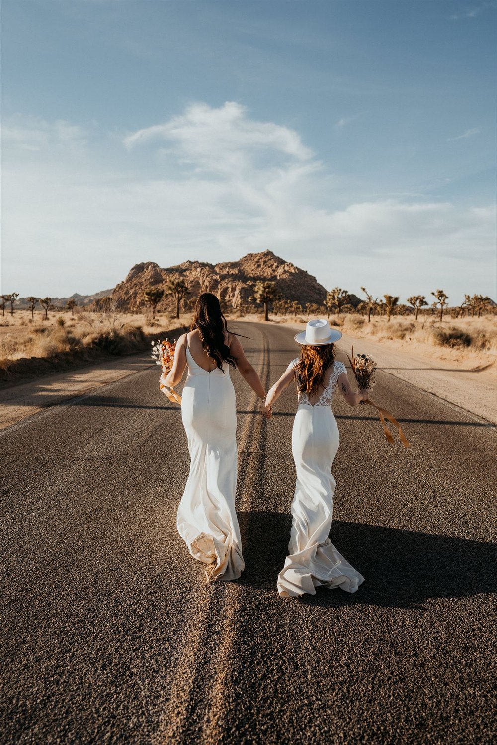 Two brides hold hands while running down the road at their California elopement in Joshua Tree National Park