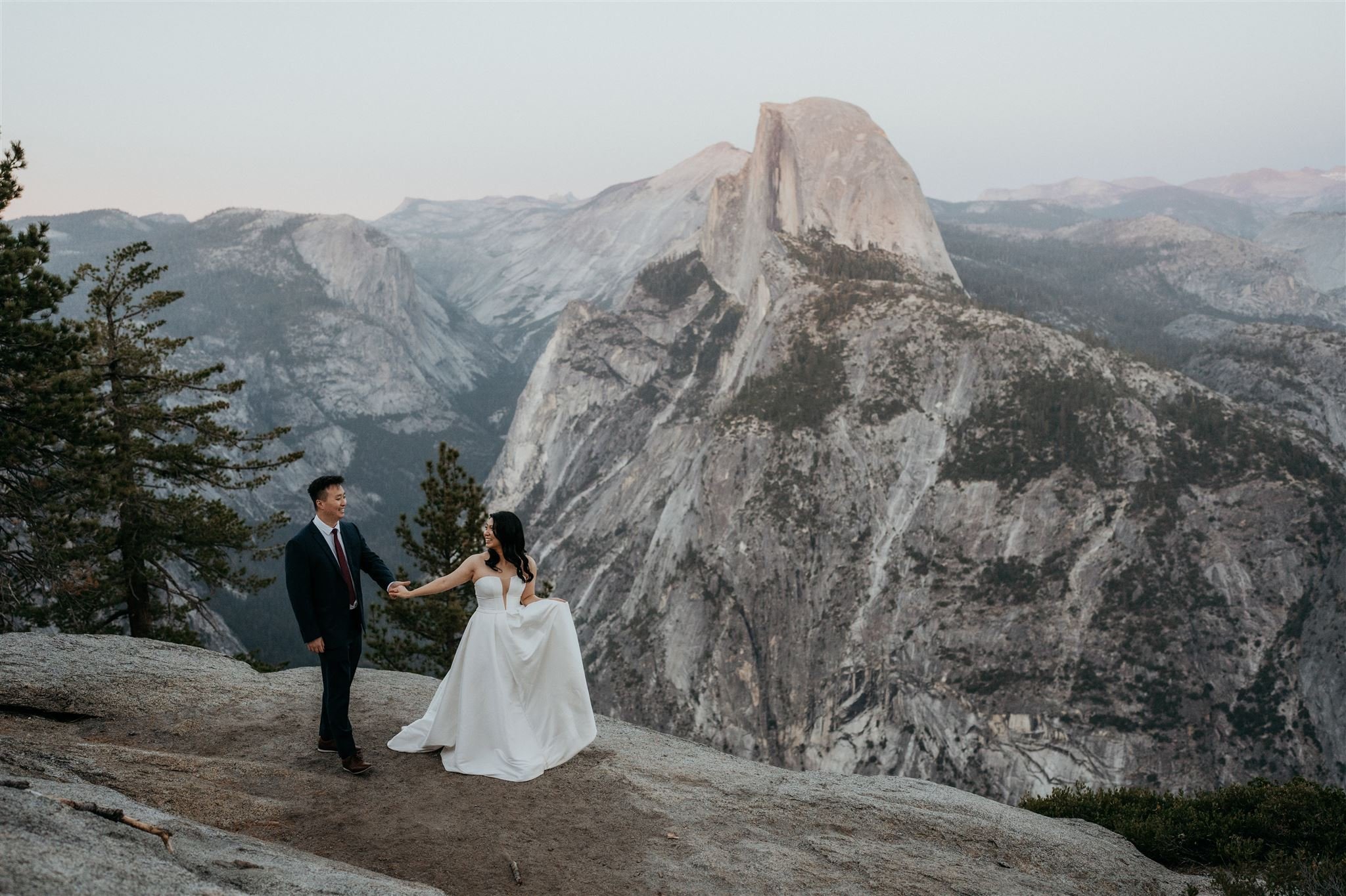 Bride and groom holding hands while walking across Glacier Point at their Yosemite elopement