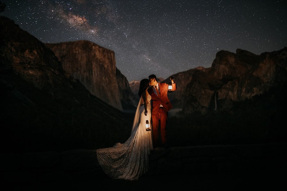 Bride and groom kiss while holding lanterns at their Yosemite elopement at Tunnel View