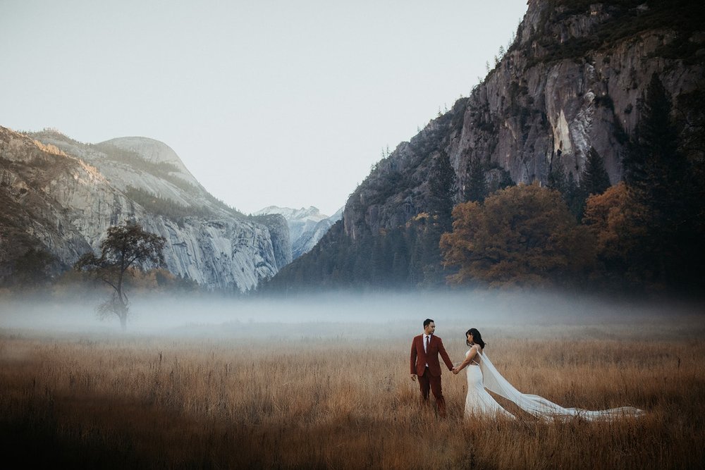 Bride and groom walk through a foggy meadow at El Capitan meadow