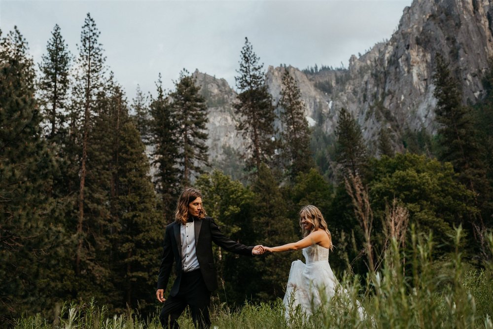 Bride and groom hold hands while walking through El Capitan meadow 