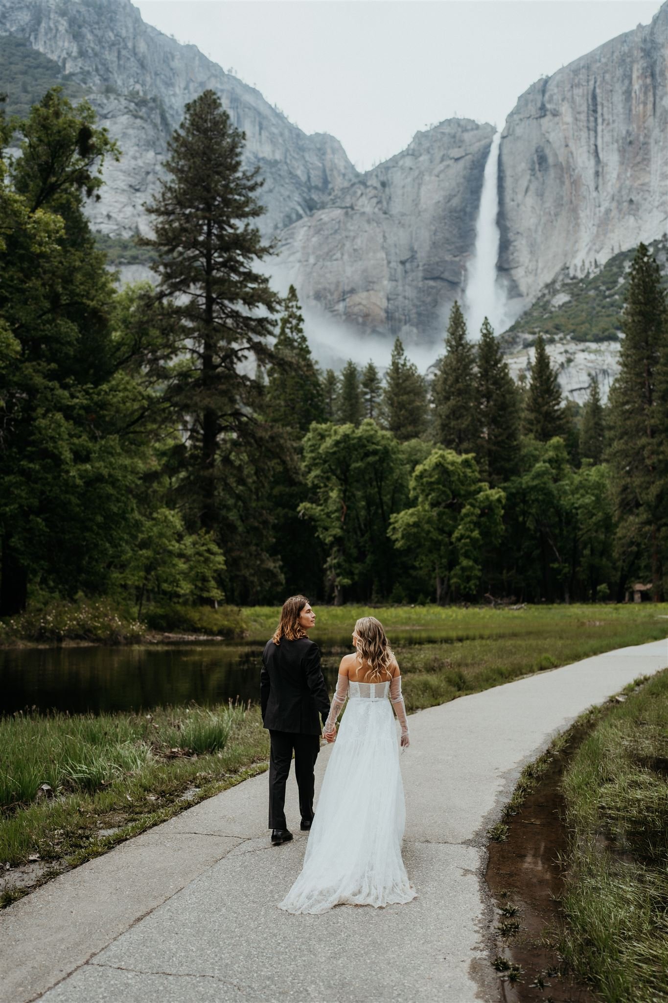 Bride and groom hold hands while walking towards Yosemite Falls