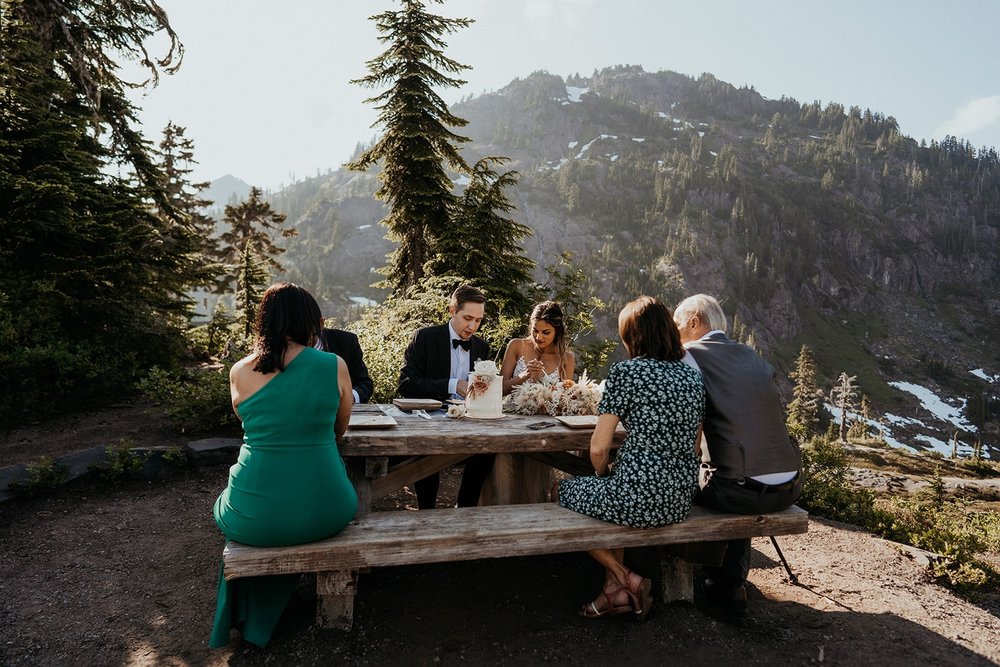 Elopements guests eat cake at a picnic table with bride and groom 