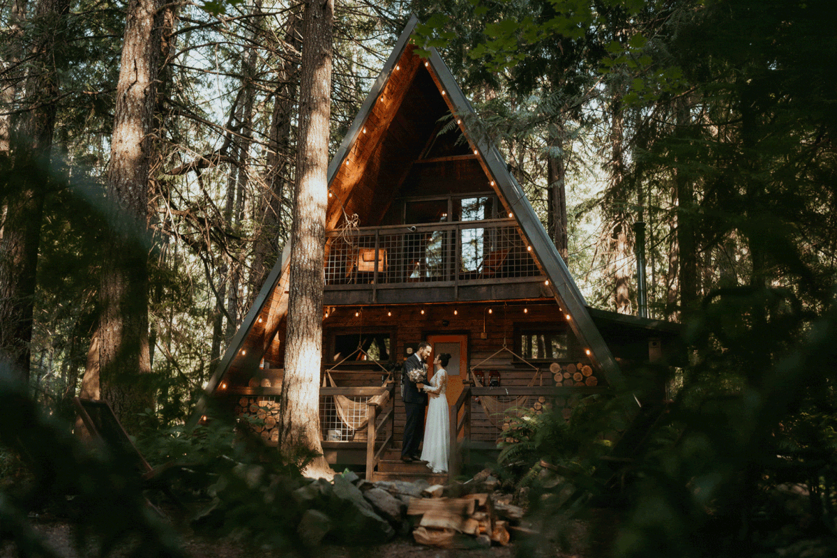 Bride and groom kiss in front of A-frame cabin during Mount Rainier elopement