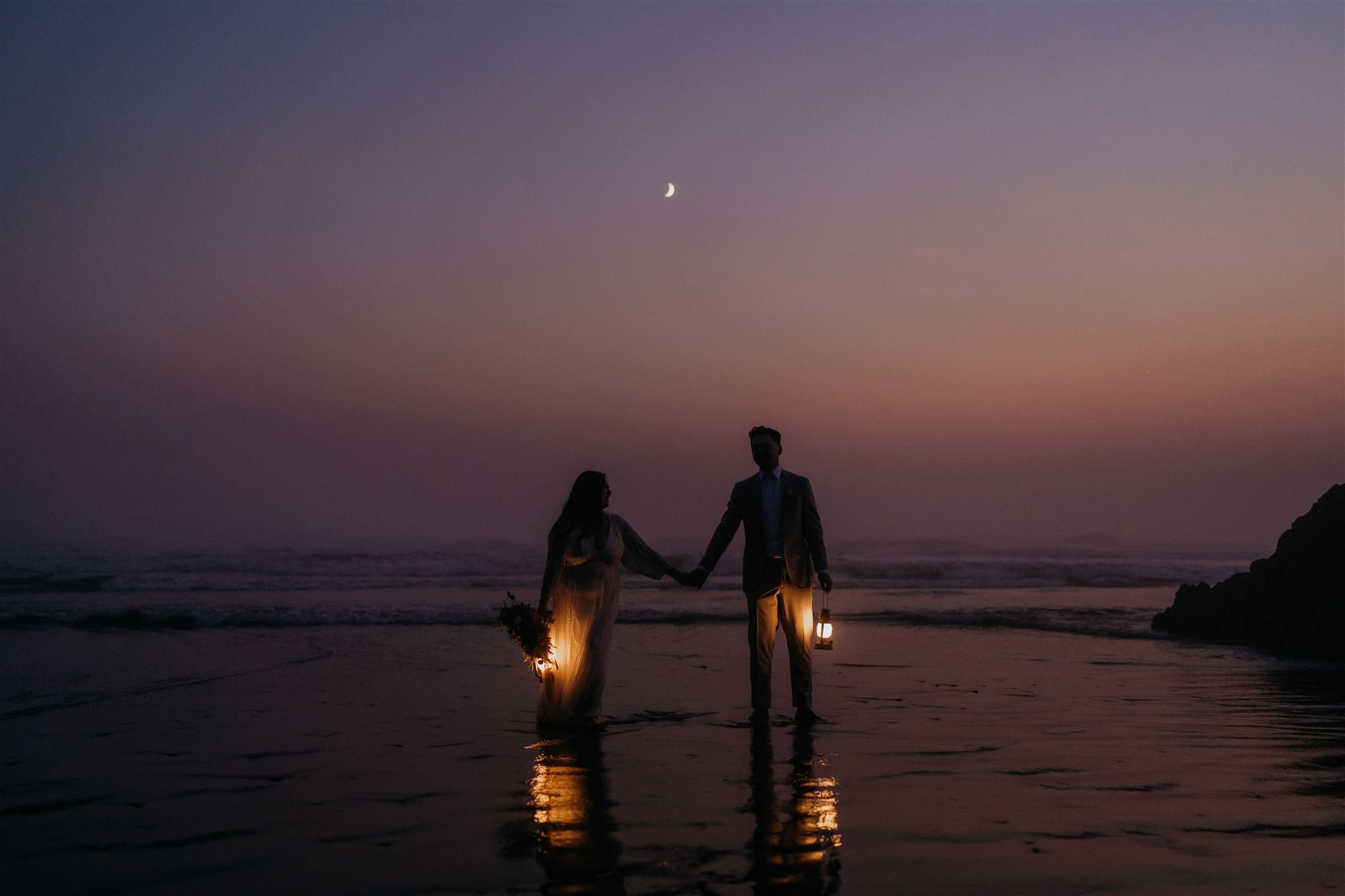 Bride and groom holding lanterns at Ruby Beach during blue hour