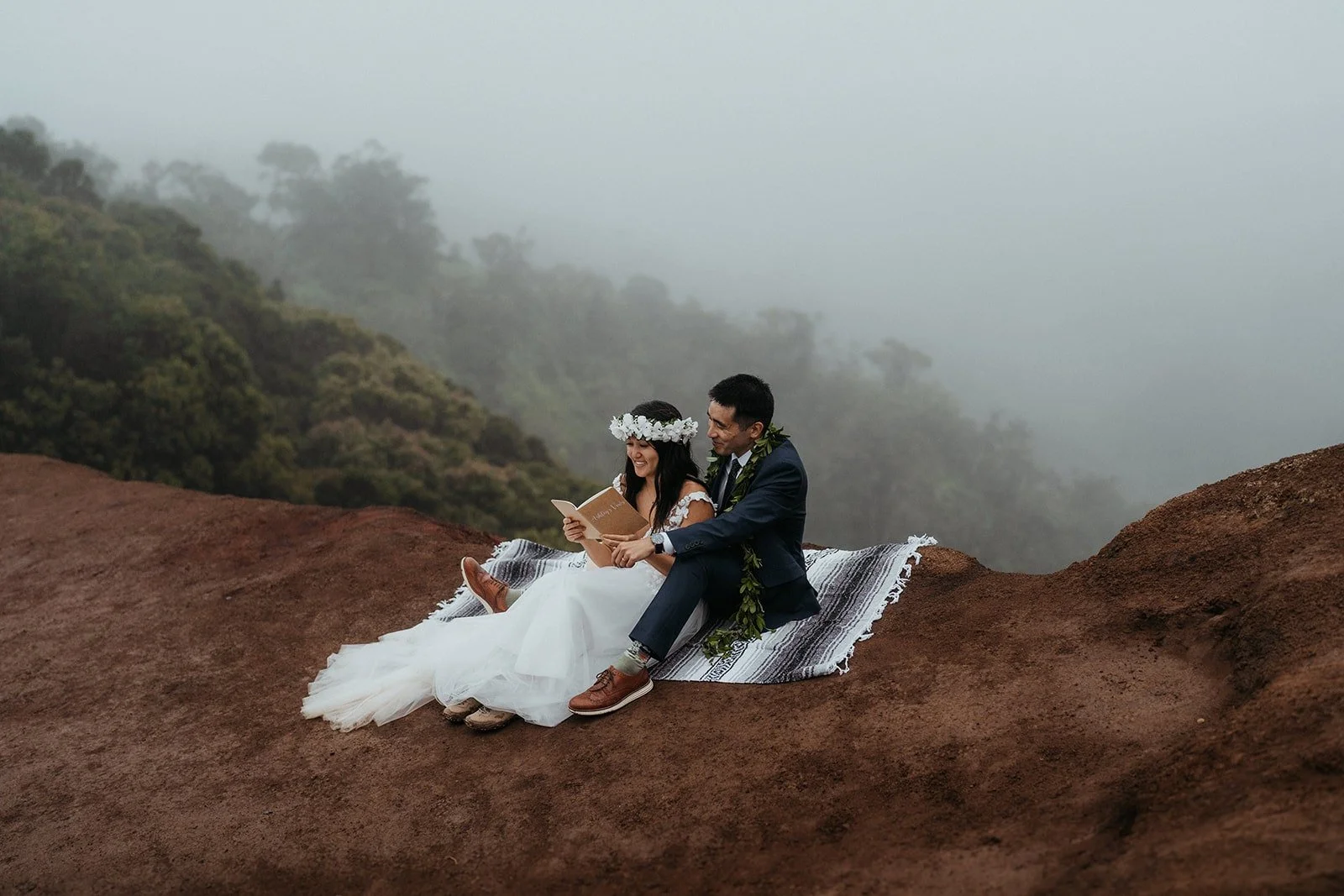 Bride and groom sit on a blanket reading letters during their Kauai Hawaii elopement