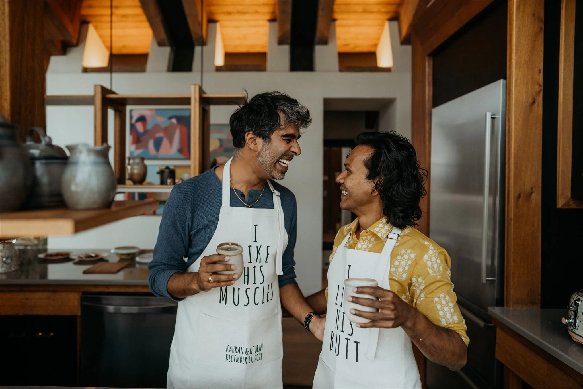 Two groom laughing and drinking tea in the kitchen on their elopement day