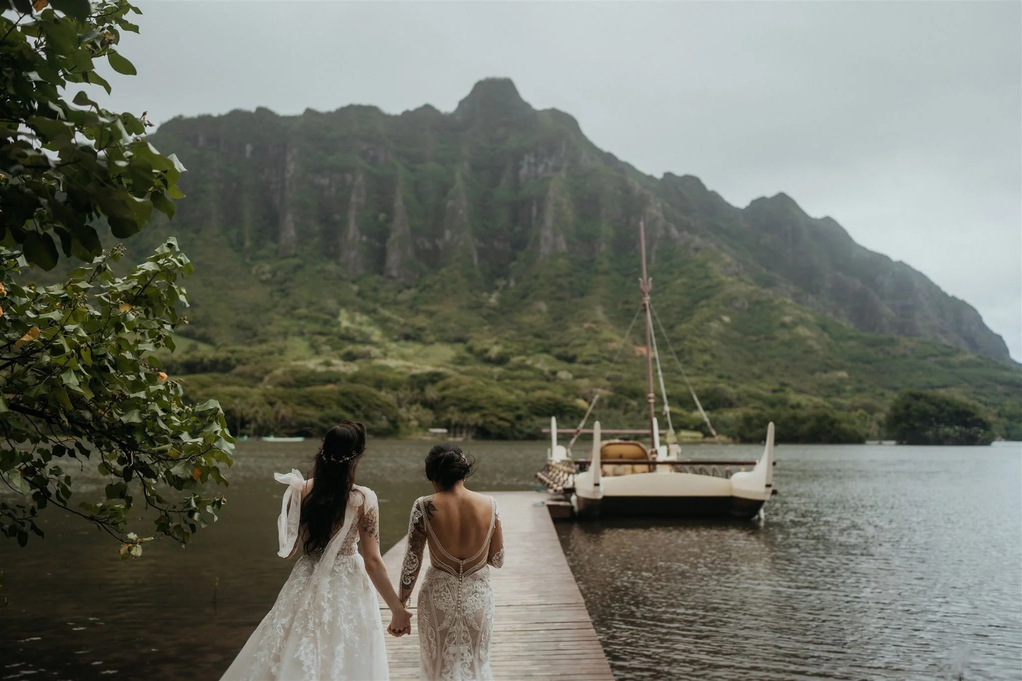 Two brides hold hands while walking down the dock for their Oahu elopement