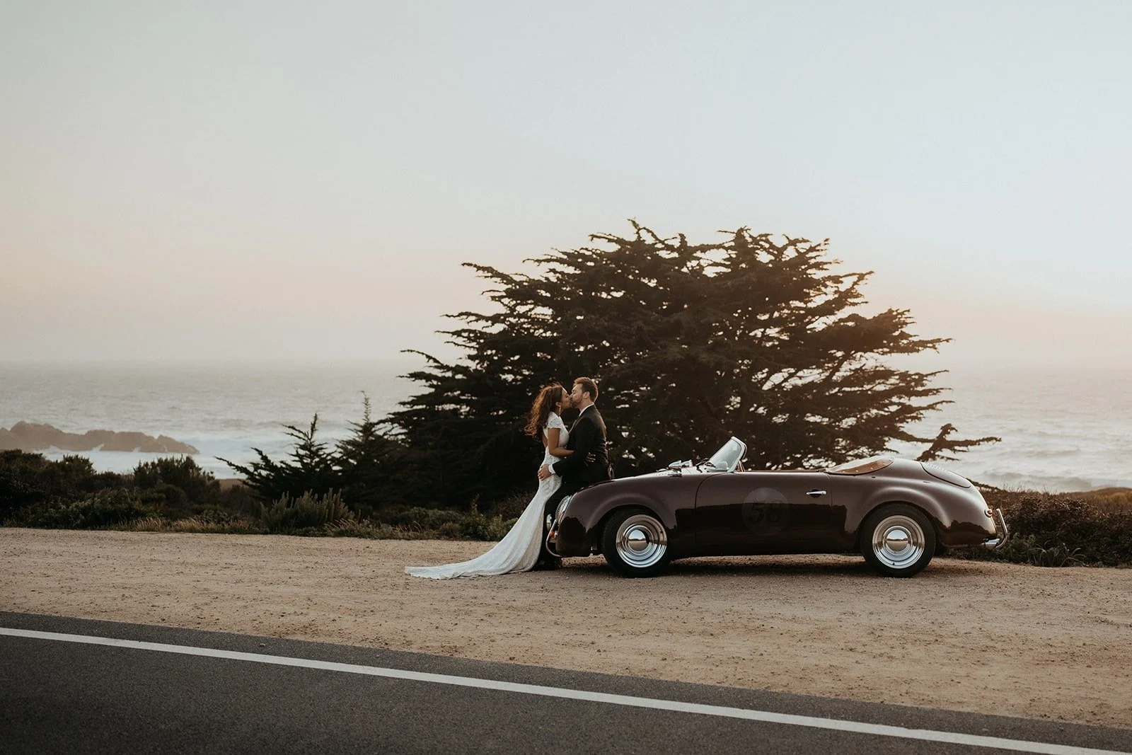 Bride and groom kiss in front of a vintage car during their elopement in Big Sur