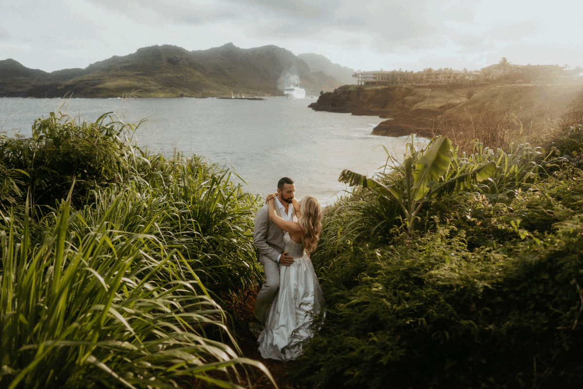 Bride and groom kiss in the tall grass by the ocean during their Hawaii elopement