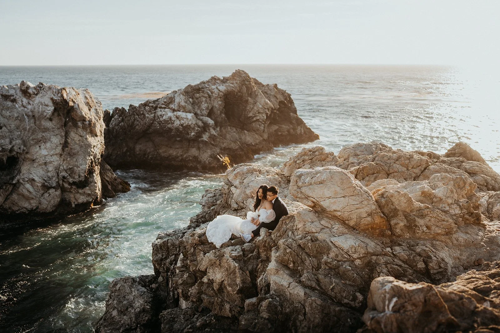 Bride and groom sit on the rocky coast during their Big Sur elopement photo session