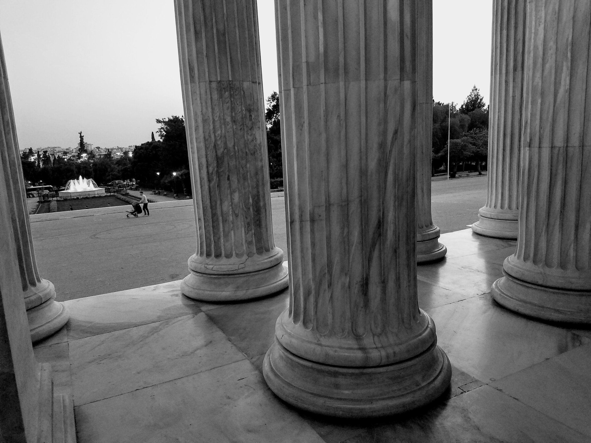Black and white photo of stone columns with a distant fountain and park view..
