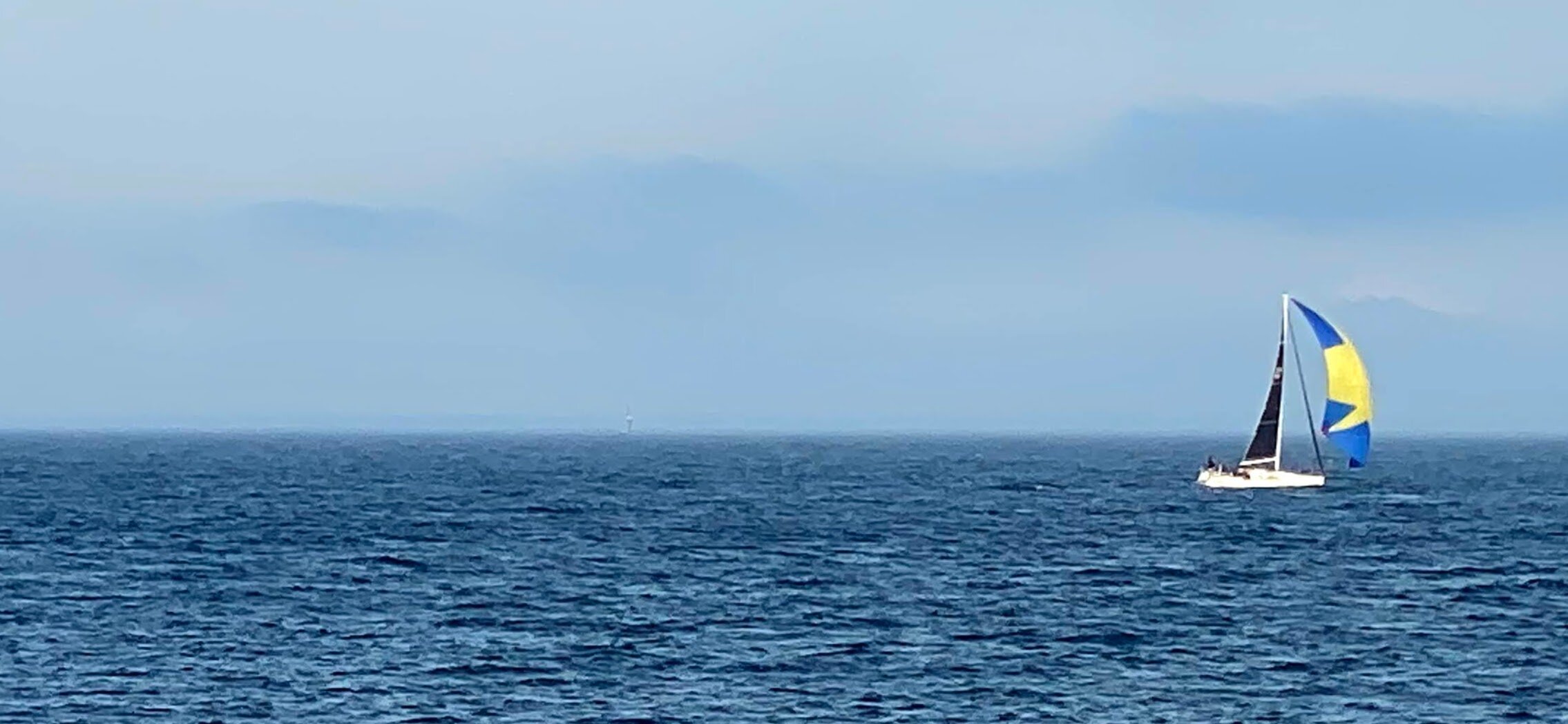 Sailboat with blue and yellow spinnaker on open sea