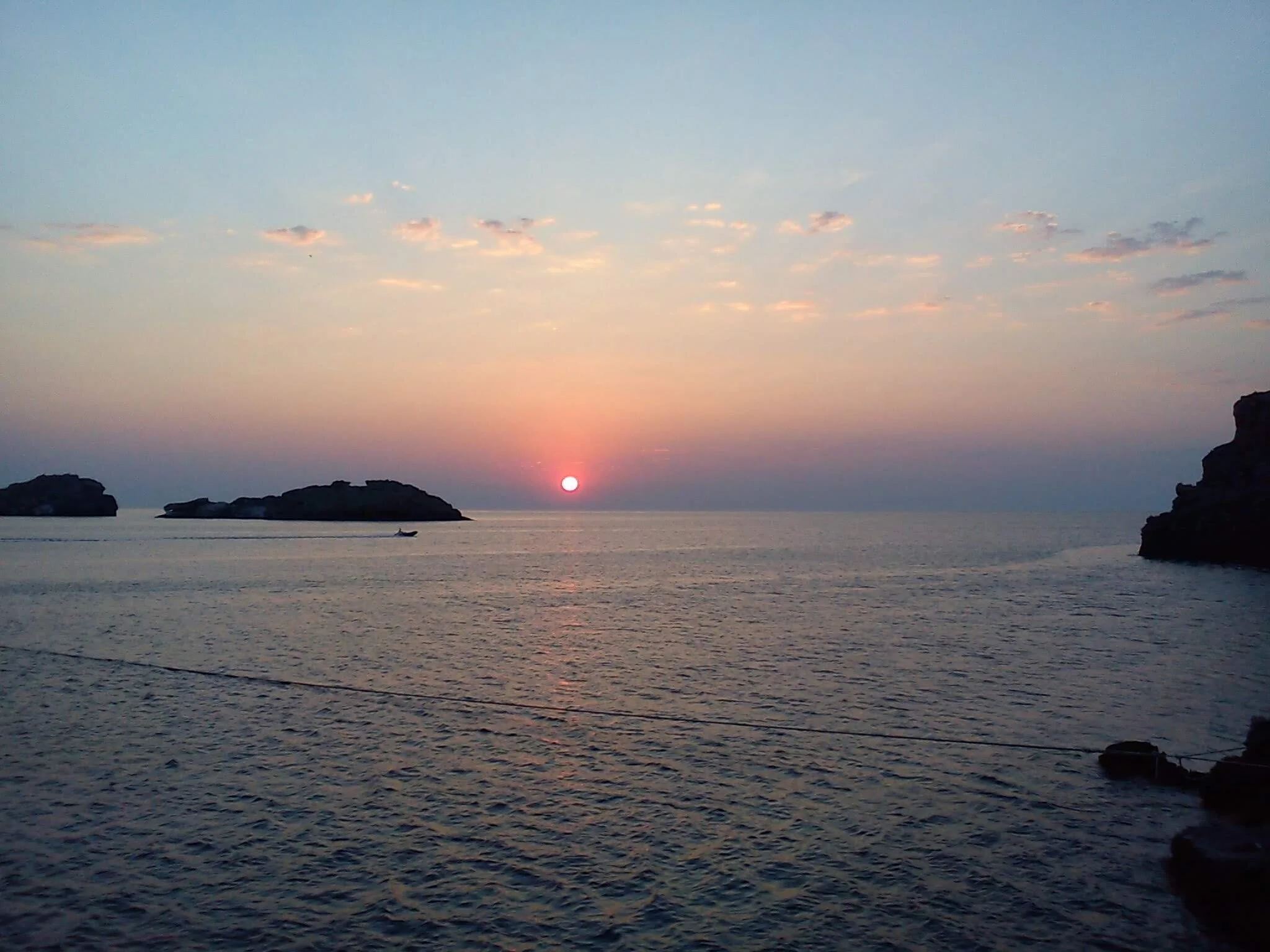 sunset over the sea with islands and a boat