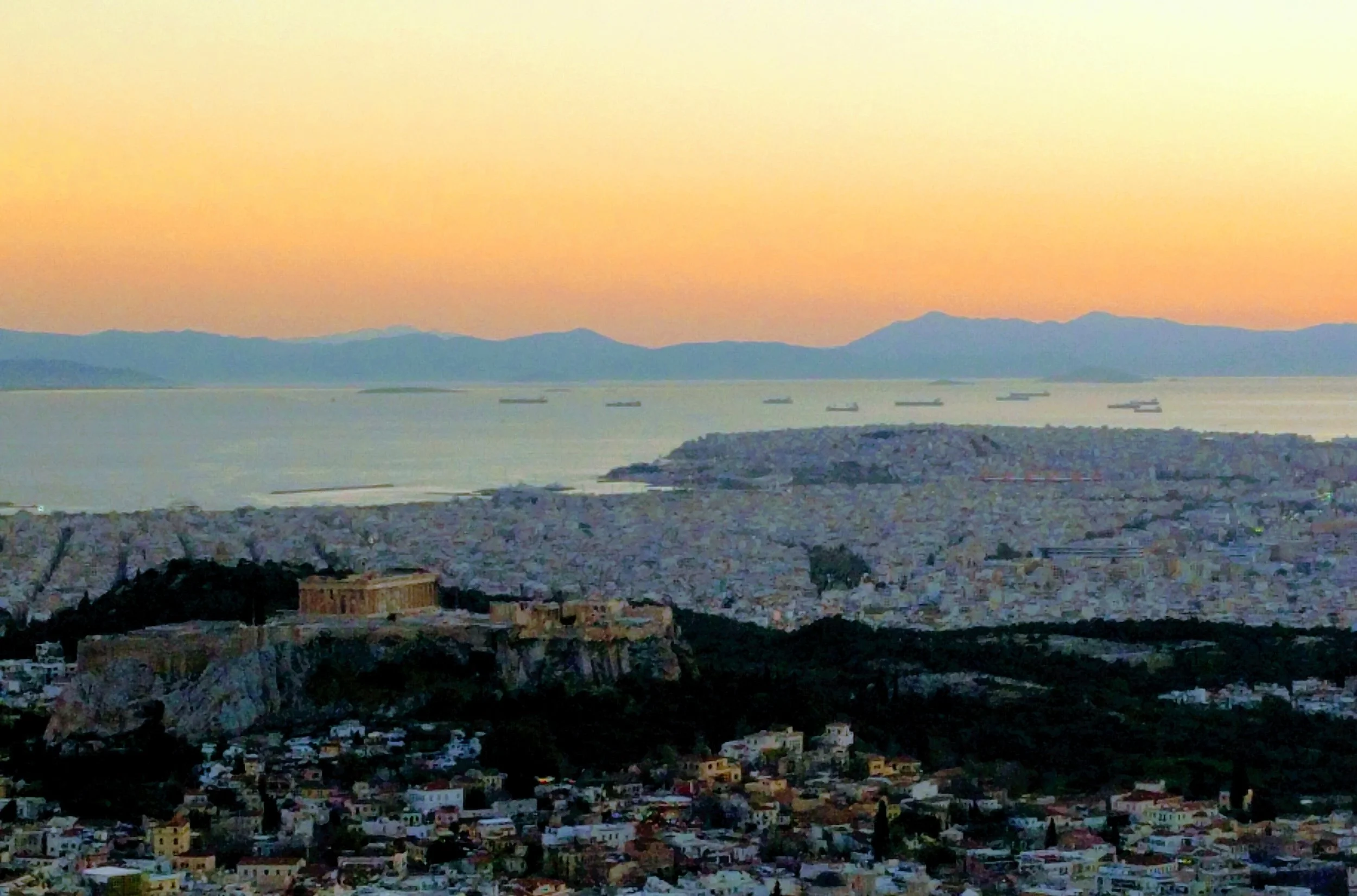 View of the Acropolis in Athens, Greece at sunset with cityscape and sea background.