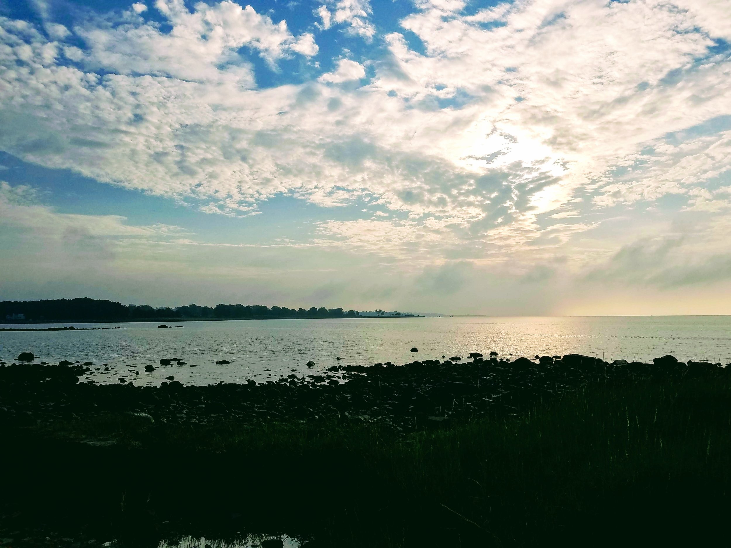 Rocky coastal landscape at sunrise with cloud-filled sky and calm sea.