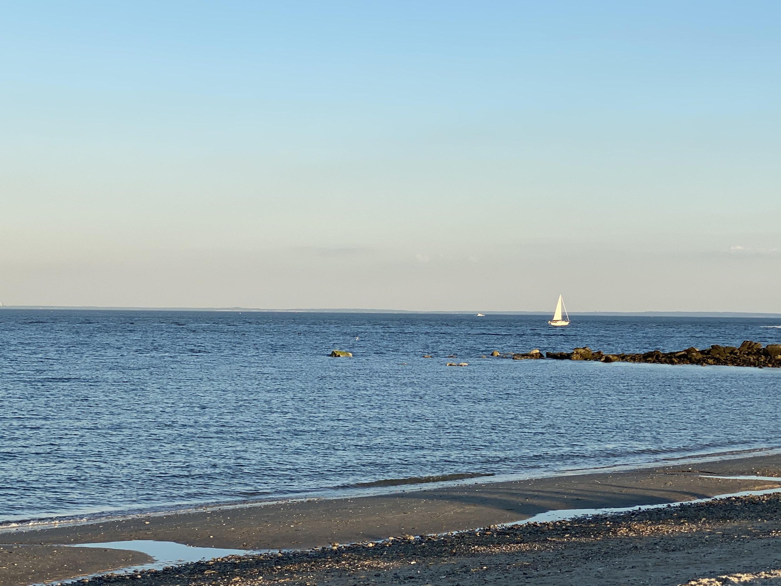 Beach scene with a sailboat on the horizon