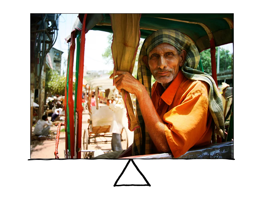 The larger Indian bike-taxi guy in the foreground is the focus, but he is balanced by the groups of people in the background. Thank goodness for him because India in the summer is HOT. 