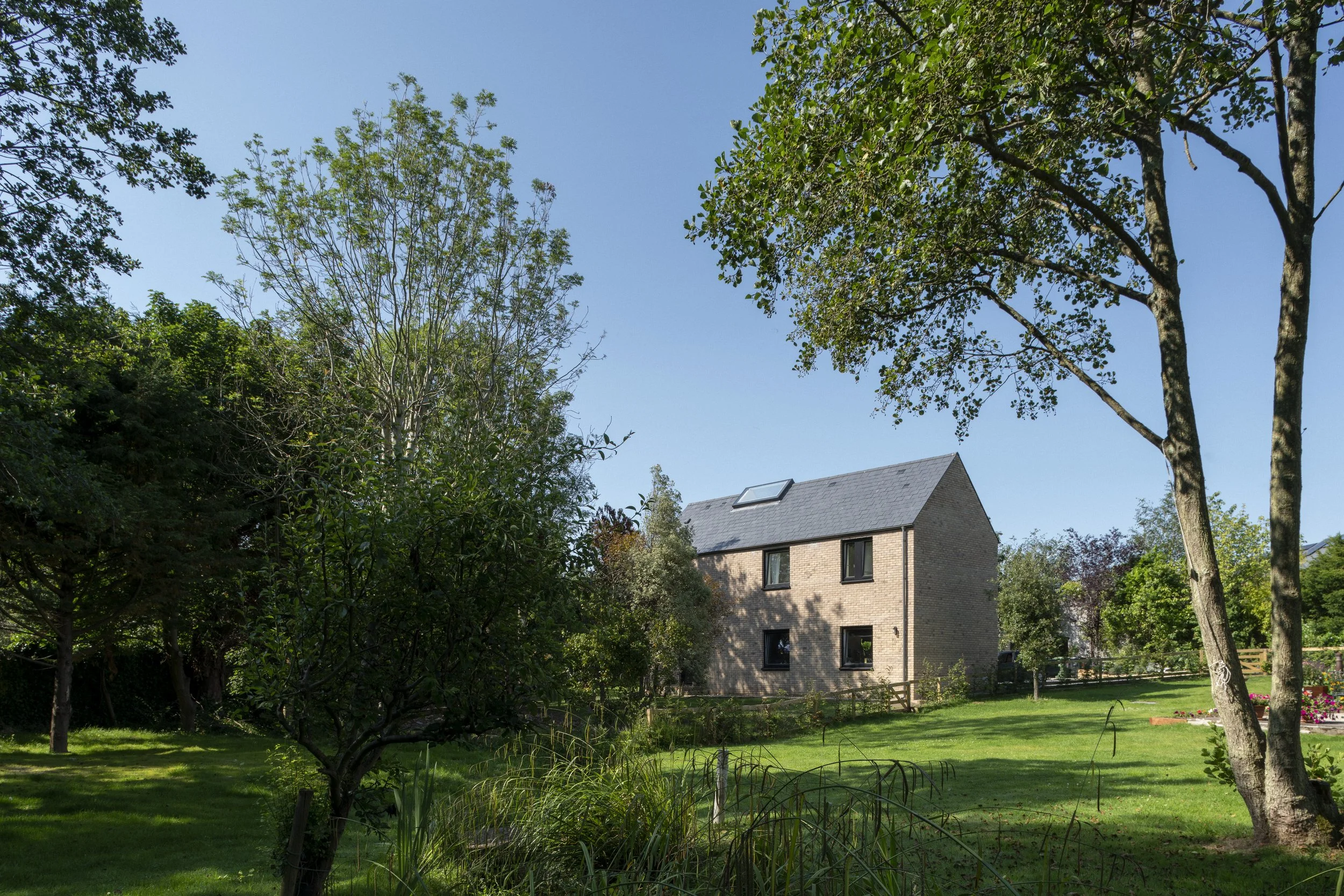 A two-story brick house with a skylight on the roof, surrounded by green trees and a well-maintained lawn under a clear blue sky.
