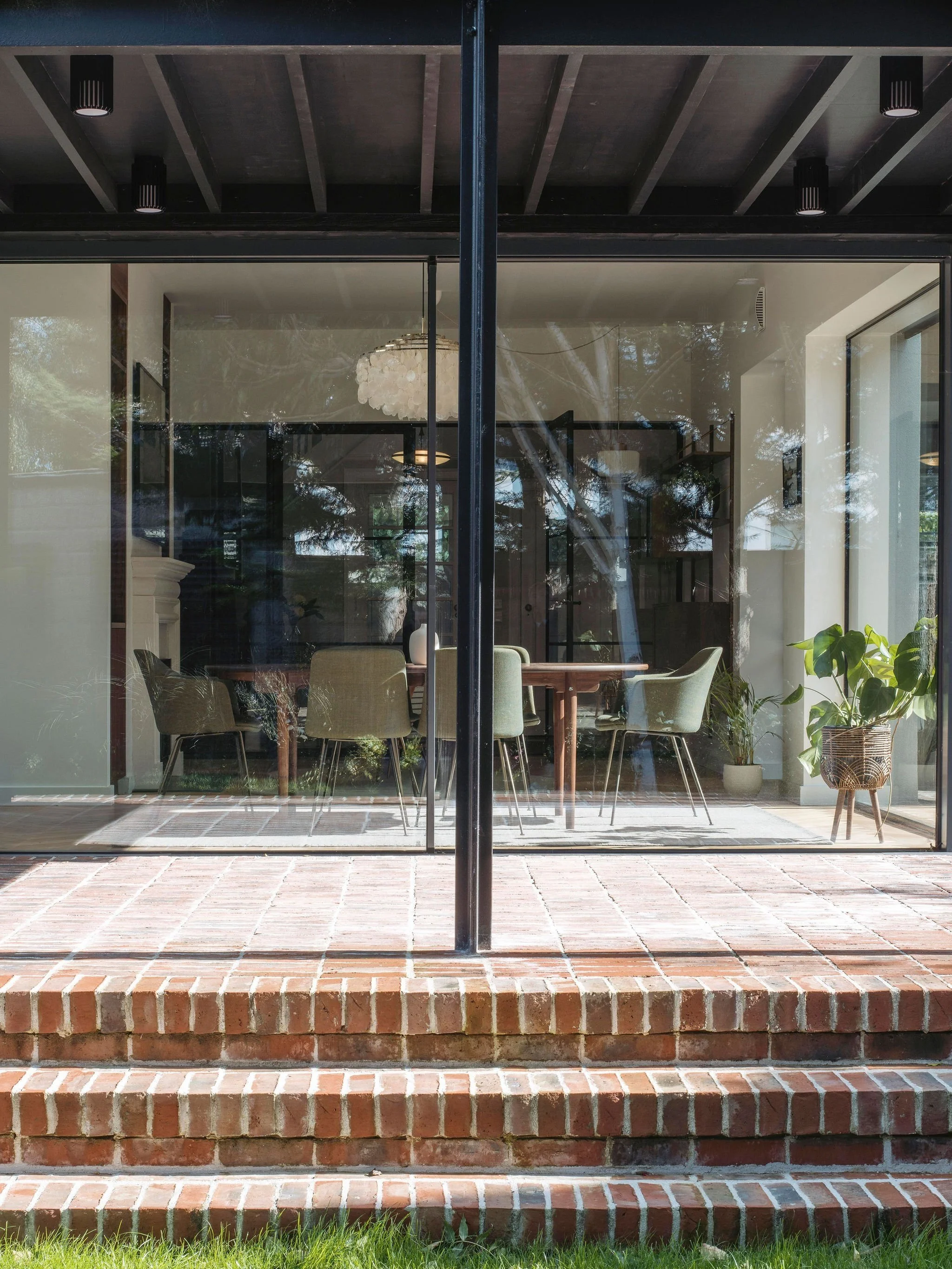 Exterior view of a modern house with large glass windows and brick steps leading to the entrance.