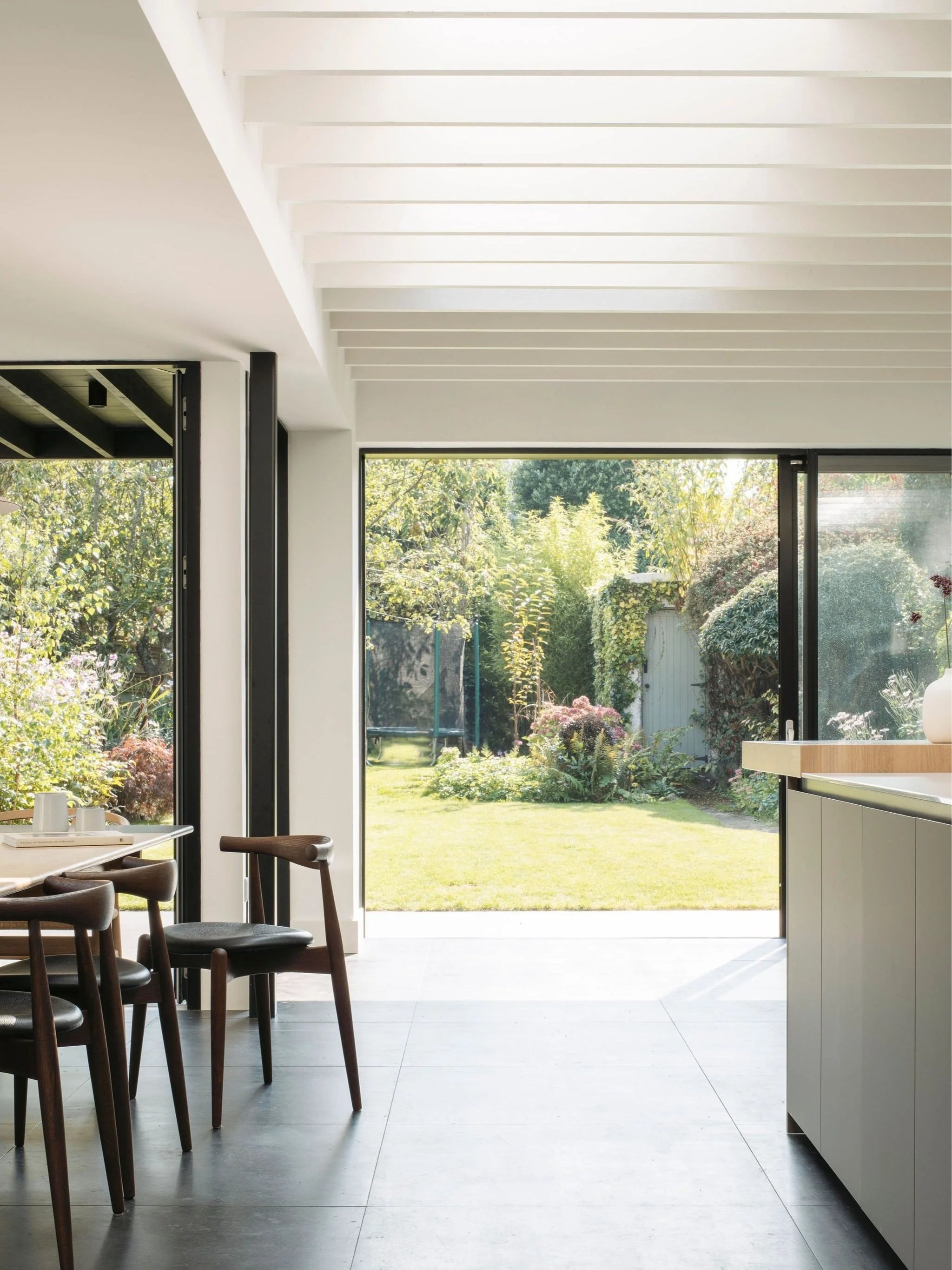 Interior of a modern kitchen with large sliding glass doors opening to a backyard garden with green grass and trees