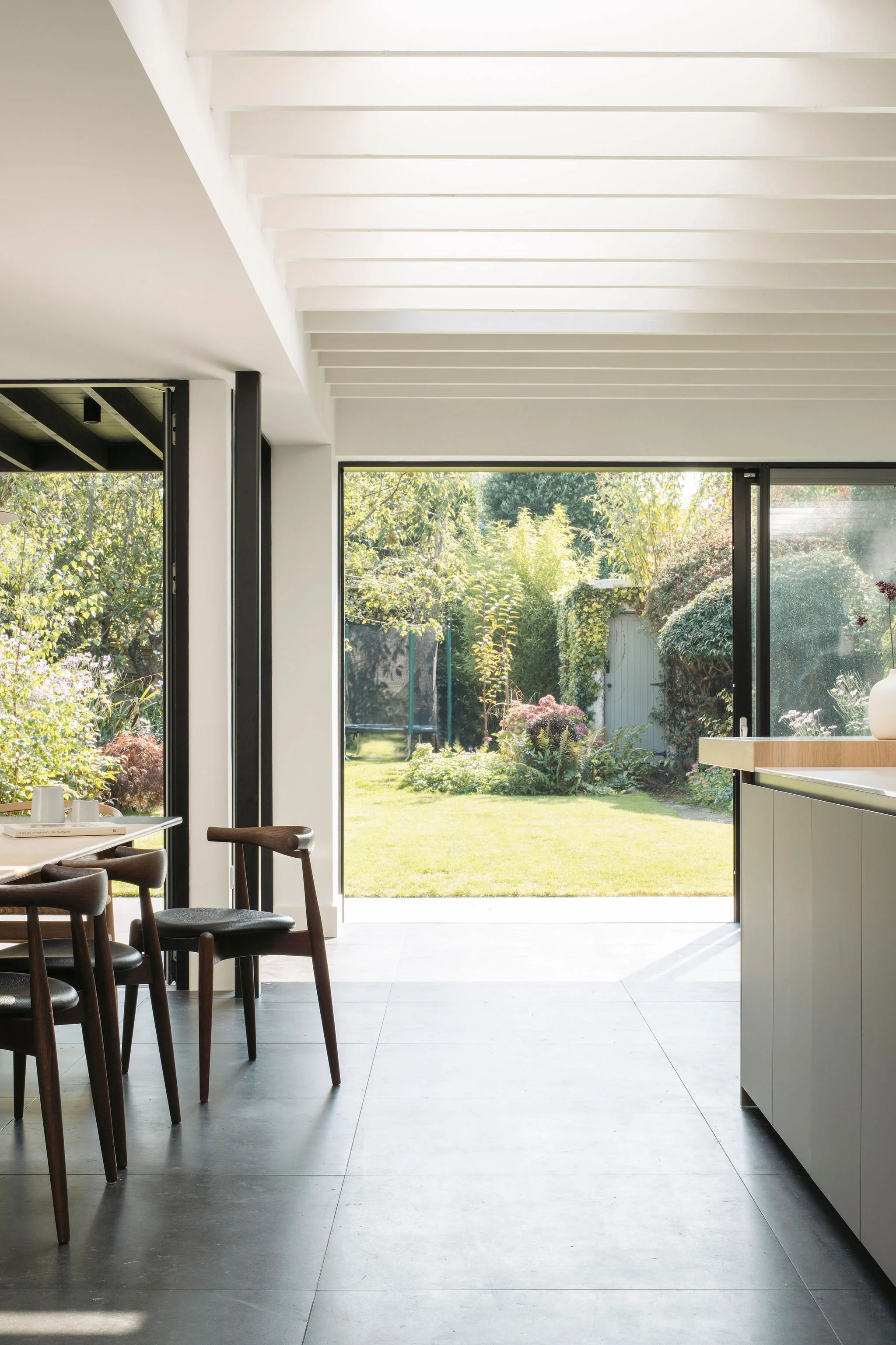 Modern kitchen with open sliding glass door leading to backyard with green lawn and garden plants.