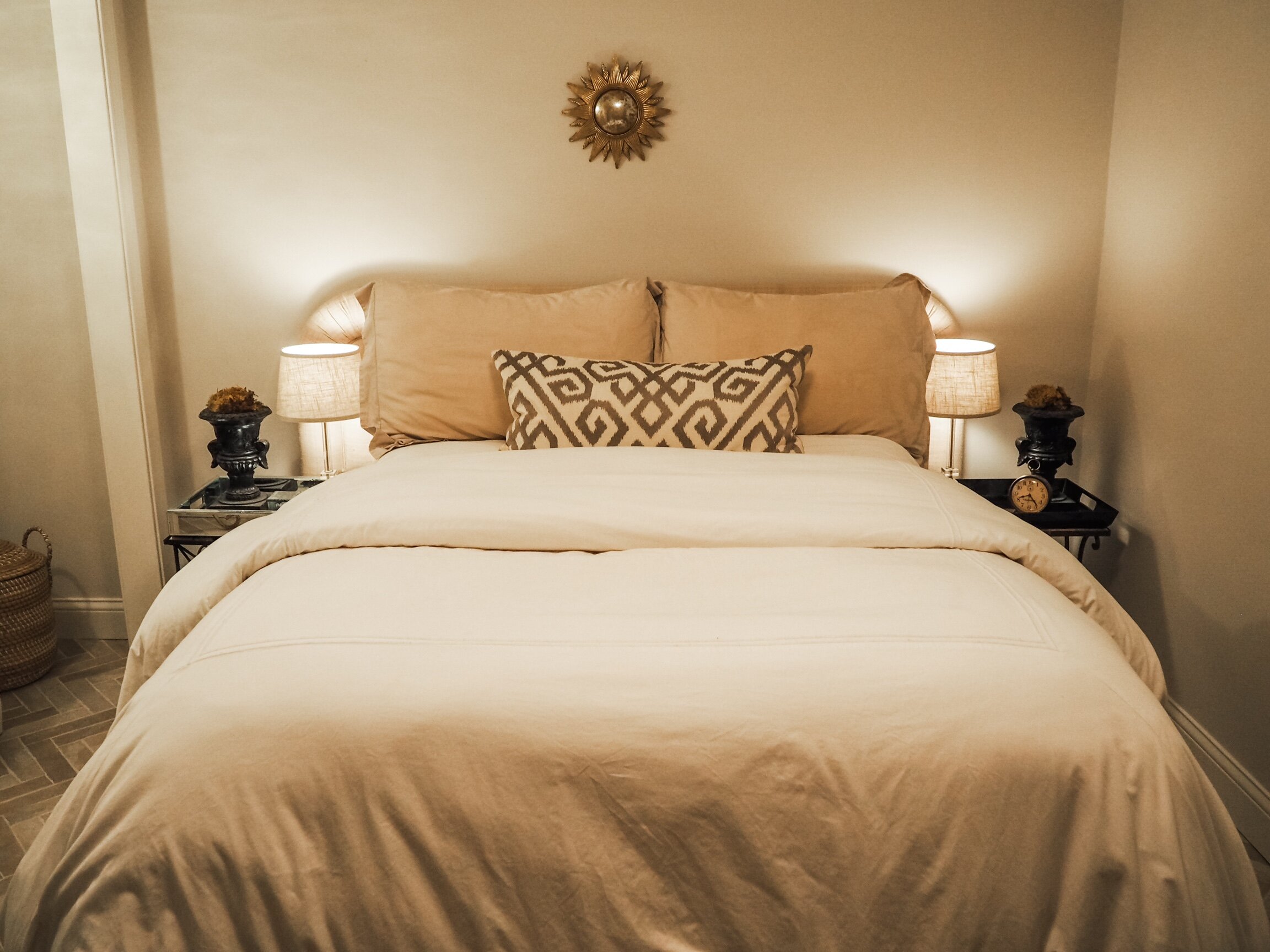 Full-sized bed and raw silk headboard, flanked by vintage crystal lamps on wrought iron nightstands