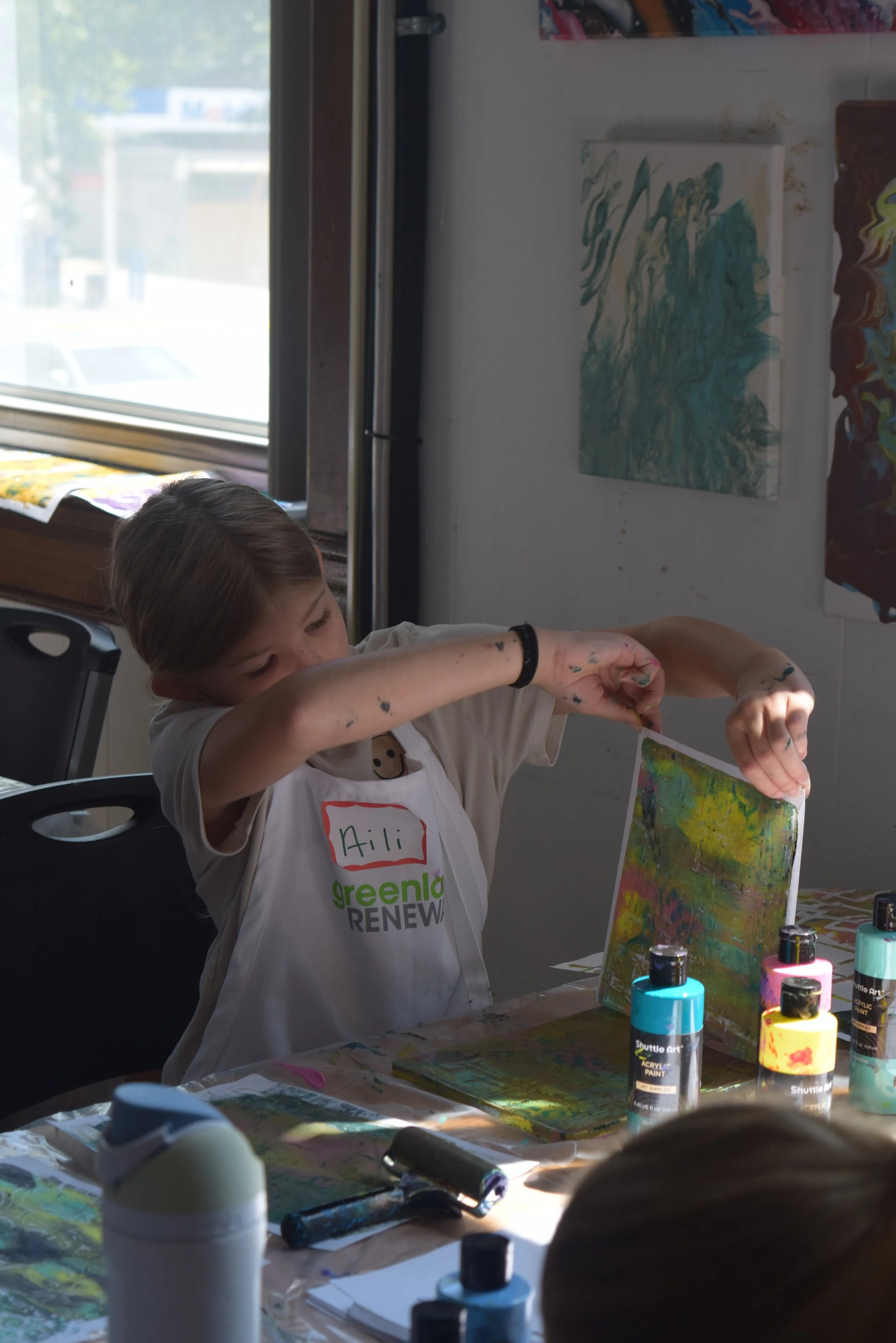 Child works on a colorful painted art project with acrylic paints during a hands-on MakerSpace activity.