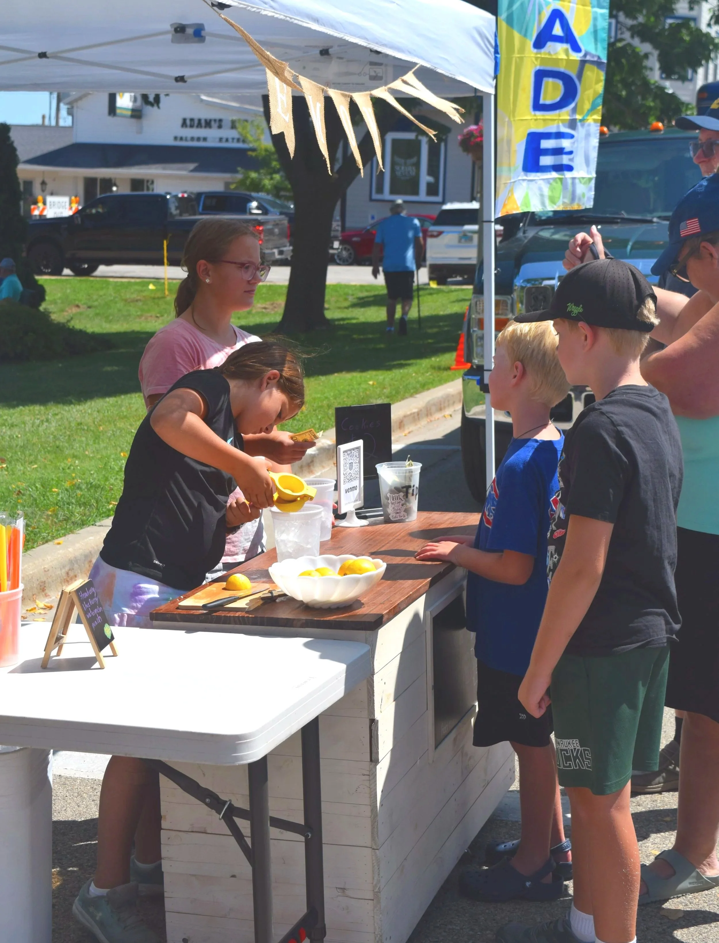 Young vendors prepare fresh lemonade for visitors at an outdoor stand during the Green Lake Fine Art Show.