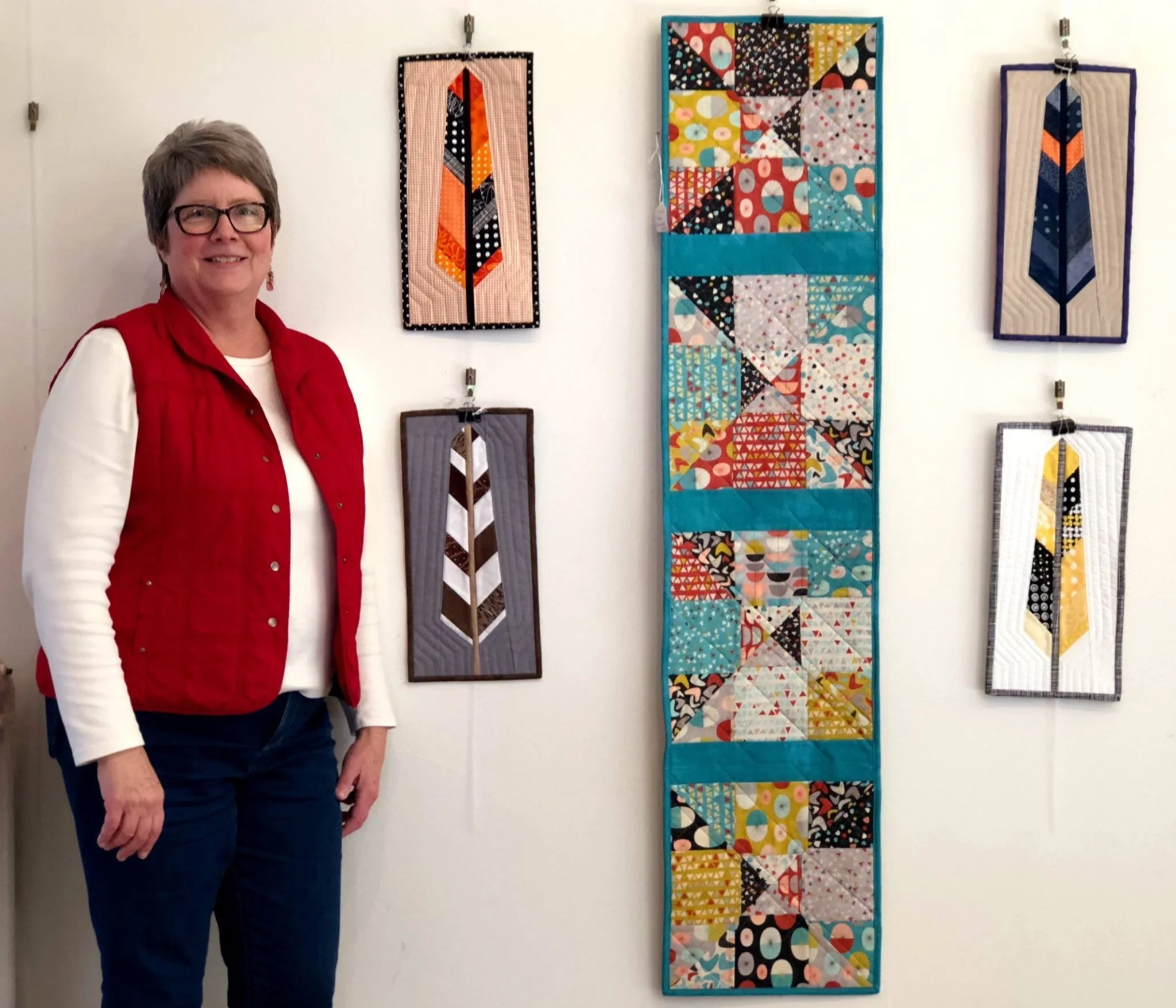 Artist standing beside a colorful display of quilted fiber art at the Town Square Lobby Art Gallery in Green Lake, Wisconsin.