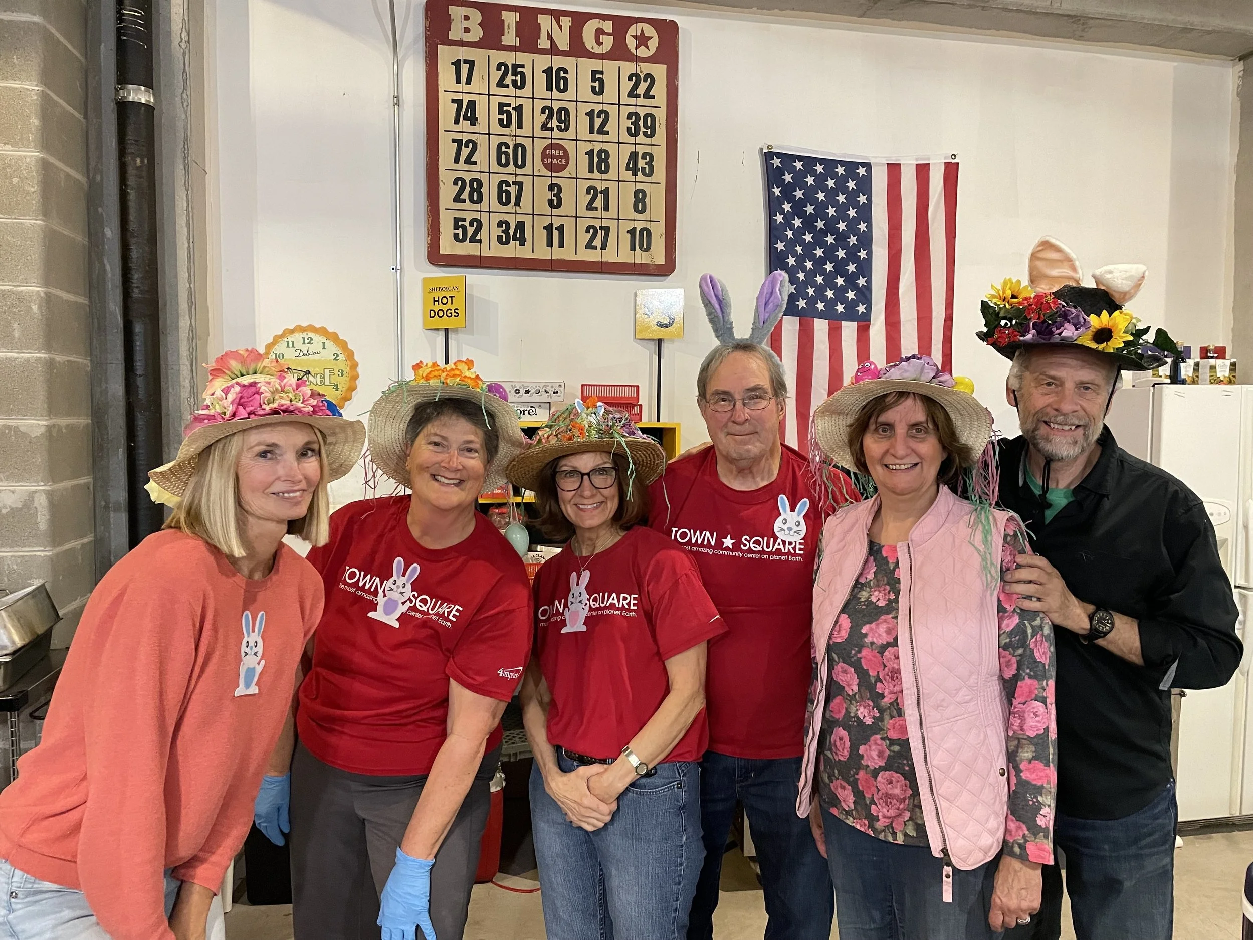 Six people wearing festive spring hats and bunny-themed shirts pose together during Town Square's Bunny Bingo.