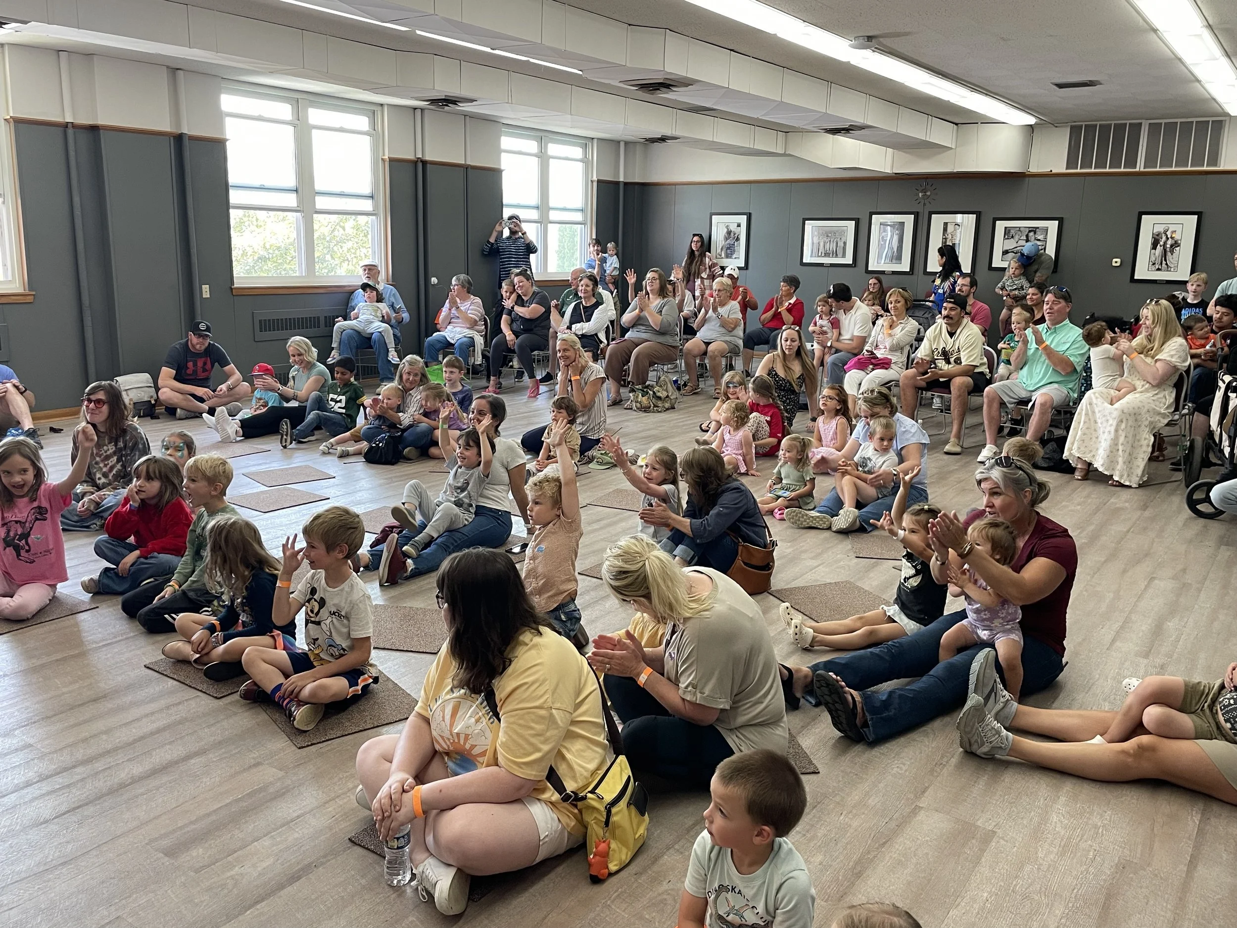 Children and parents sit in Studio A for a presentation by Dinosaur Dimensions at Dino Daze.