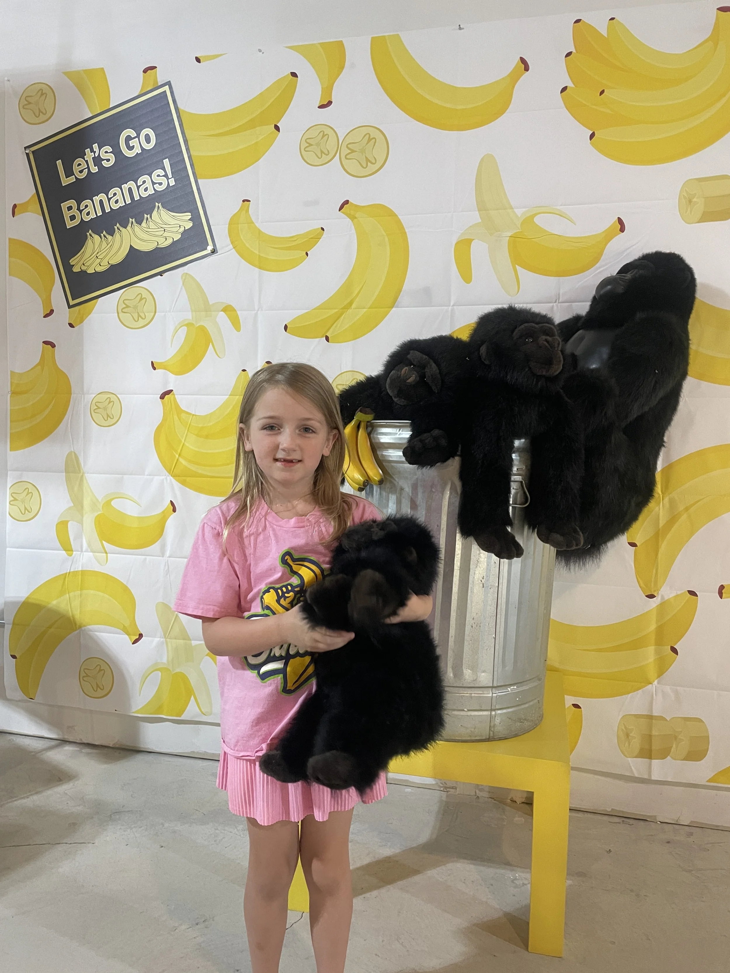 Young girl holding a stuffed gorilla in front of a banana-themed backdrop at Town Square's Go Bananas Bingo.