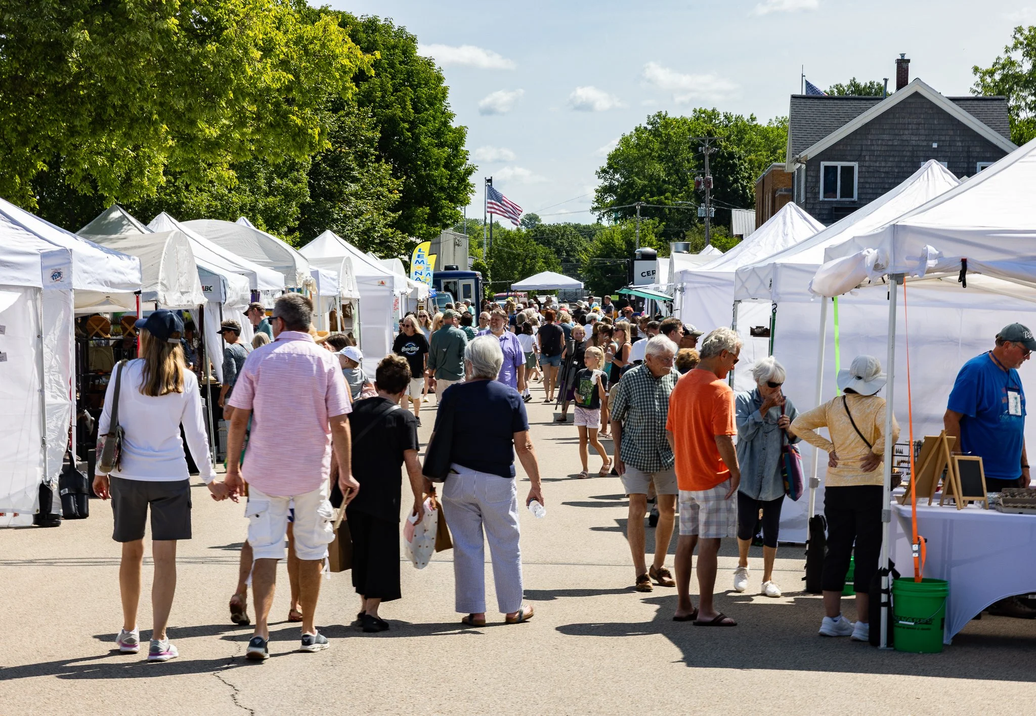 Visitors browse artwork and vendor booths beneath white tents along a downtown Green Lake street during the annual Fine Art Show.