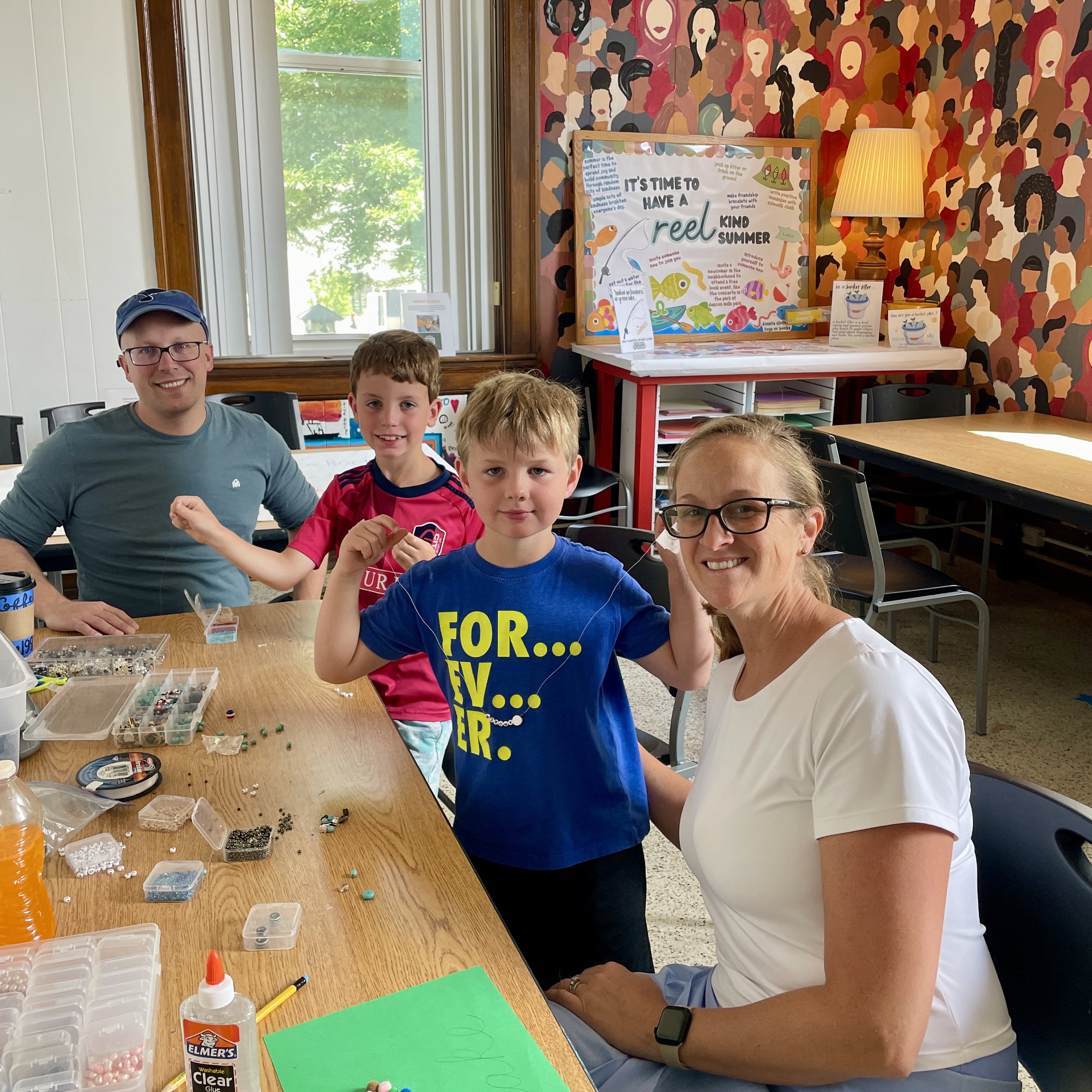 Family creates beaded jewelry together at a craft table in the MakerSpace at Town Square Community Center.
