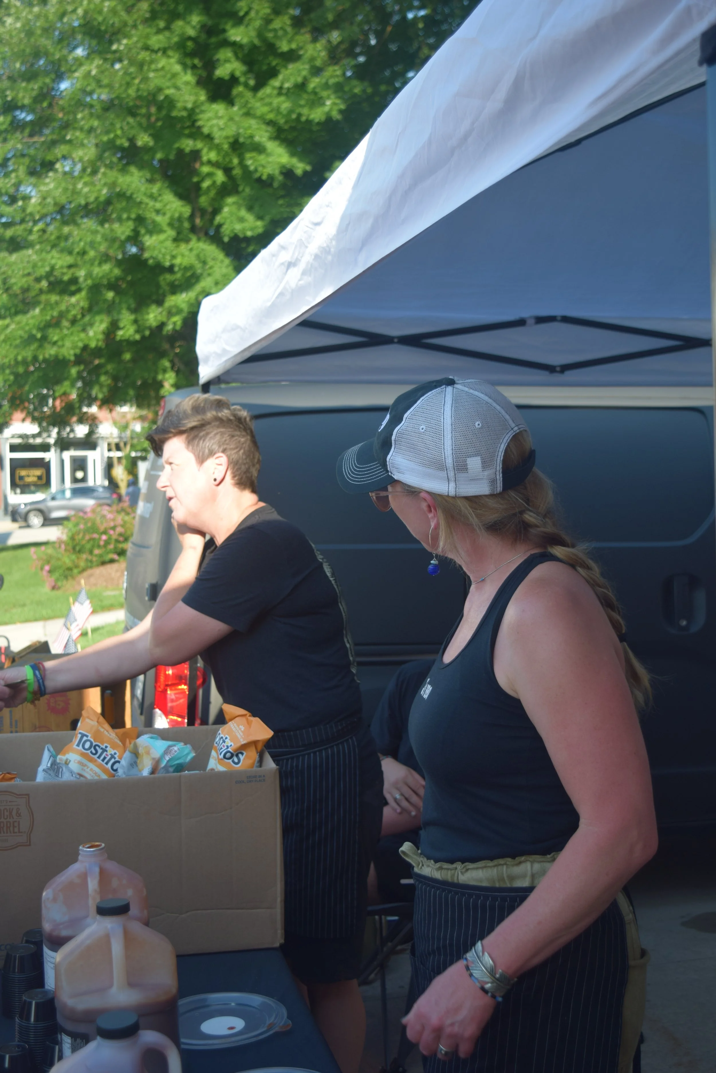 Two food vendors work beneath a tent at Party on the Pond, with drinks and snacks arranged on the serving table.