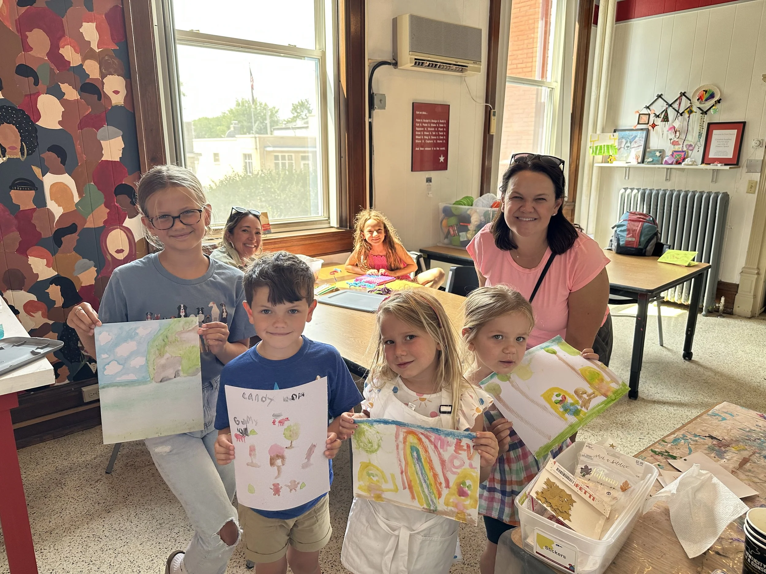Children and adults display colorful drawings and paintings created together during a family art activity in the MakerSpace.