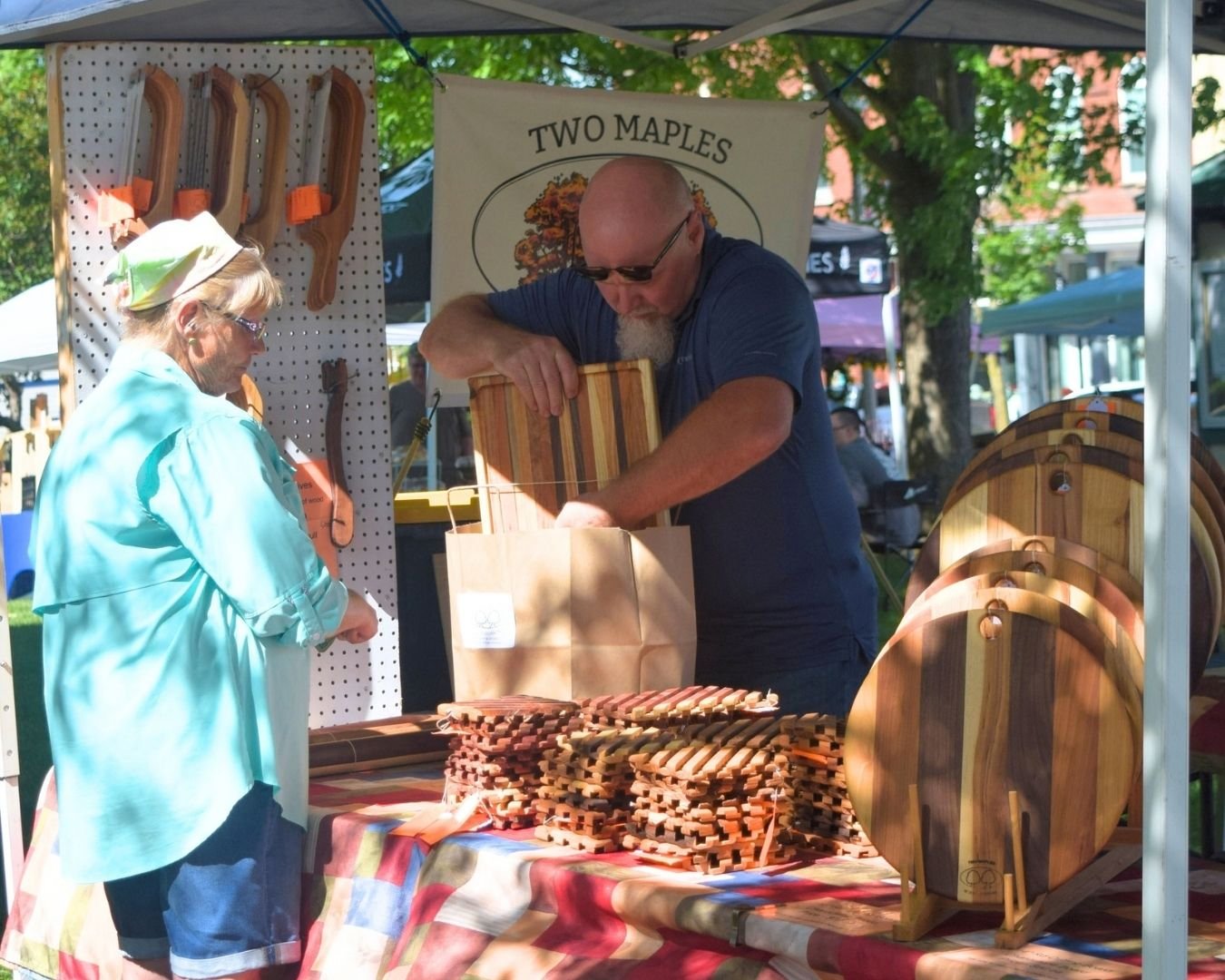 A local woodworker helps a shopper at a booth filled with handcrafted wooden items at the Town Square Summer Market.