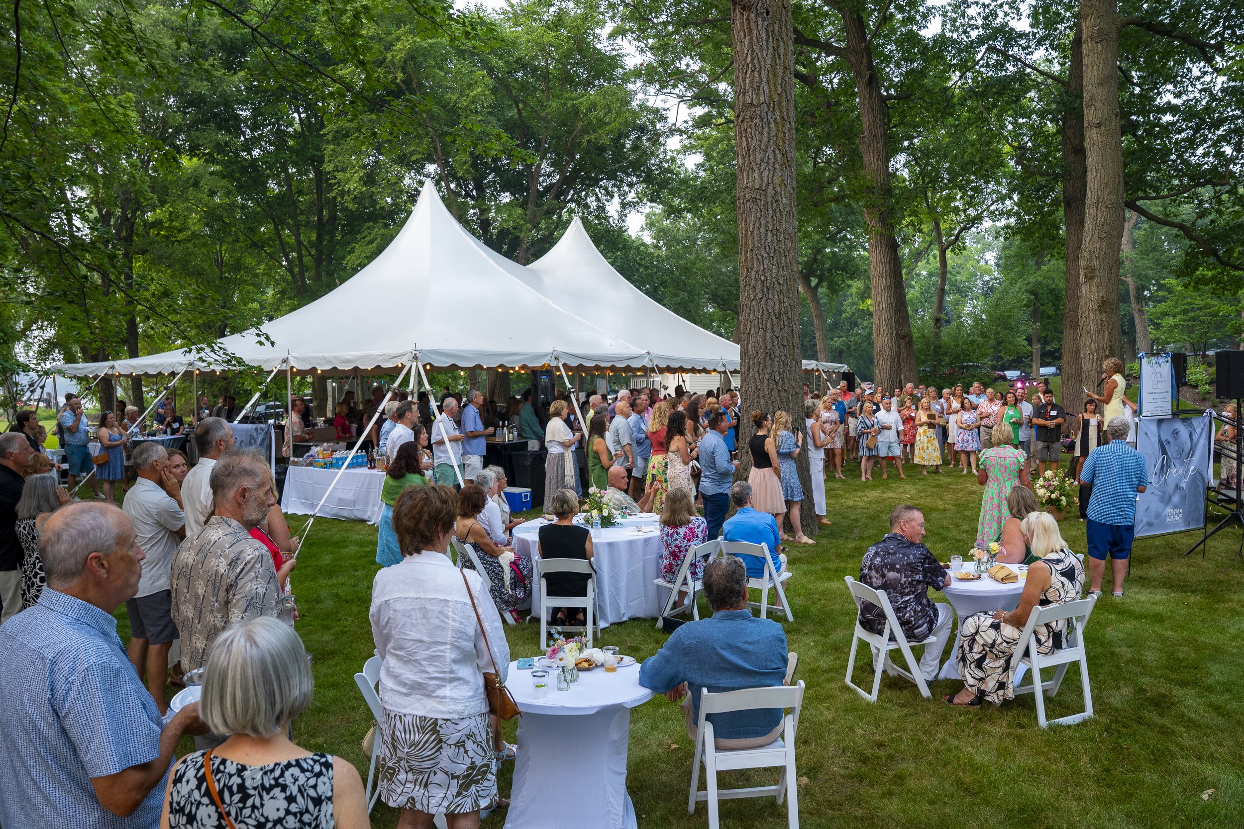 Wide view of guests gathered around cocktail tables and beneath a white tent during the outdoor Affair for the Square fundraiser in Green Lake.