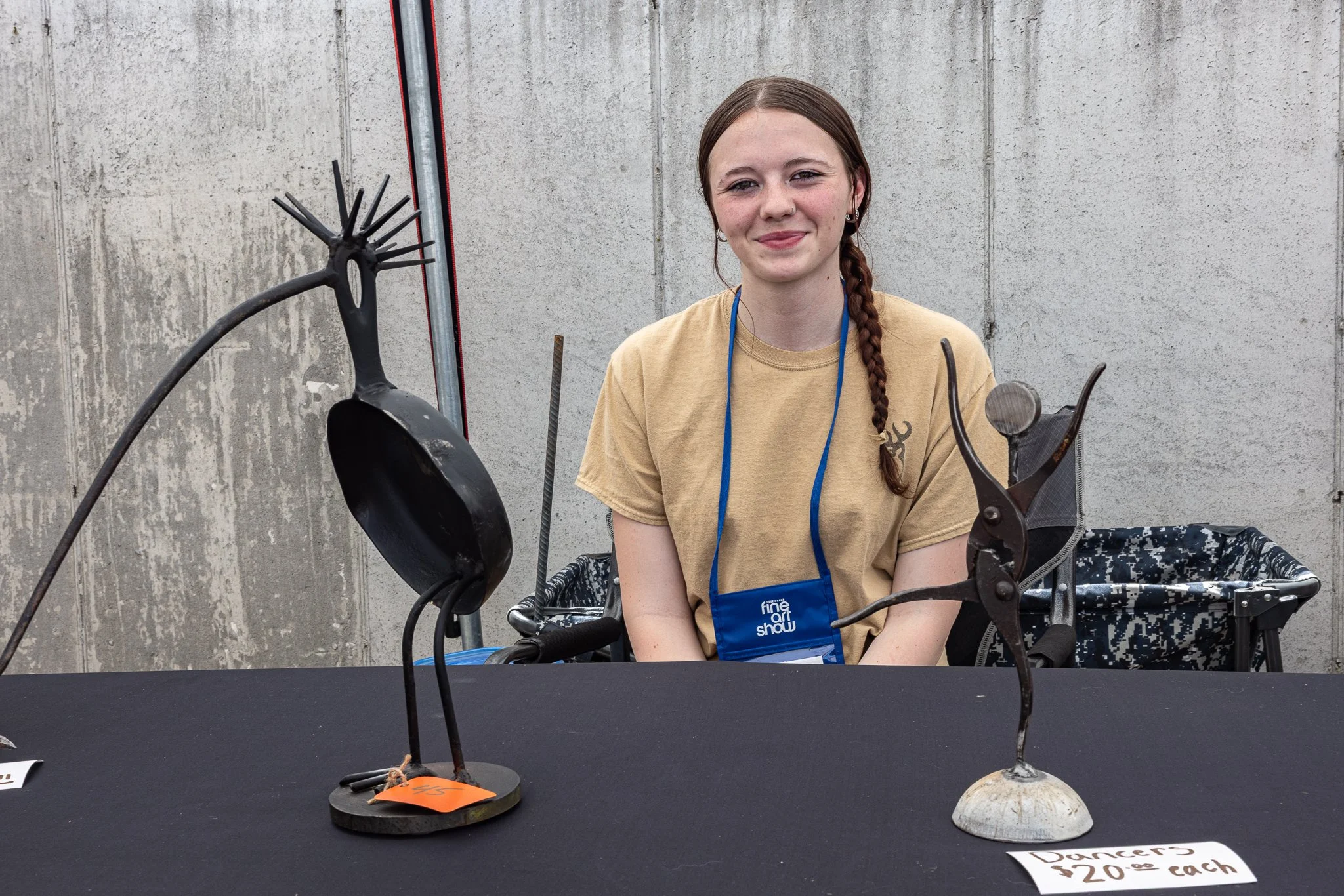 Young artist sits behind a display of handcrafted metal bird sculptures at the Green Lake Fine Art Show.