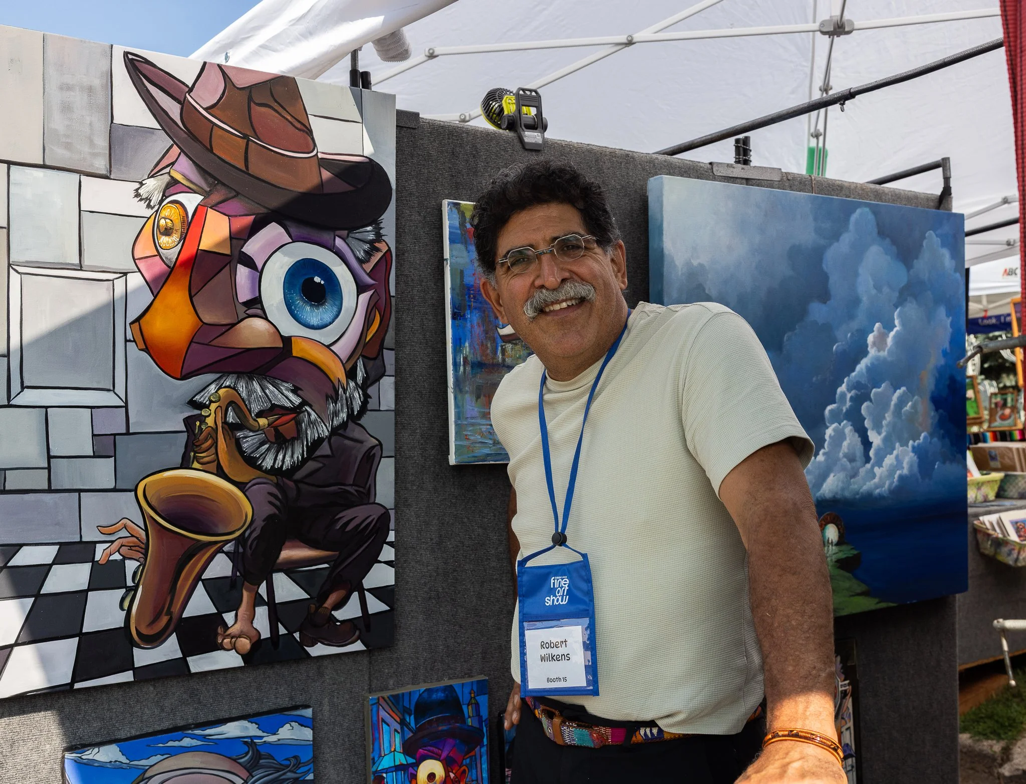 Artist Robert Wilkens stands beside his colorful paintings, including an abstract musician portrait, at the Green Lake Fine Art Show.
