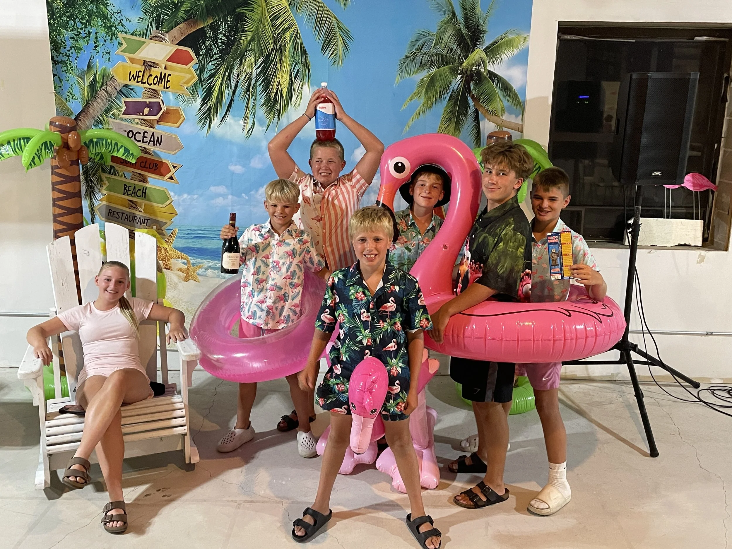 Group of young Bingo attendees posing with pink flamingo pool floats and tropical decorations at Town Square.