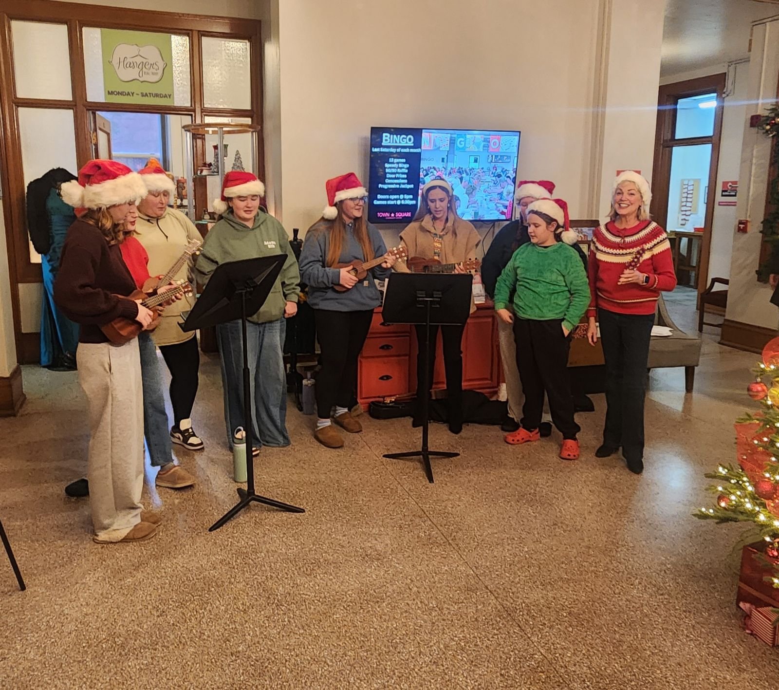Carolers wearing Santa hats sing and play instruments during a holiday celebration at Town Square Community Center.