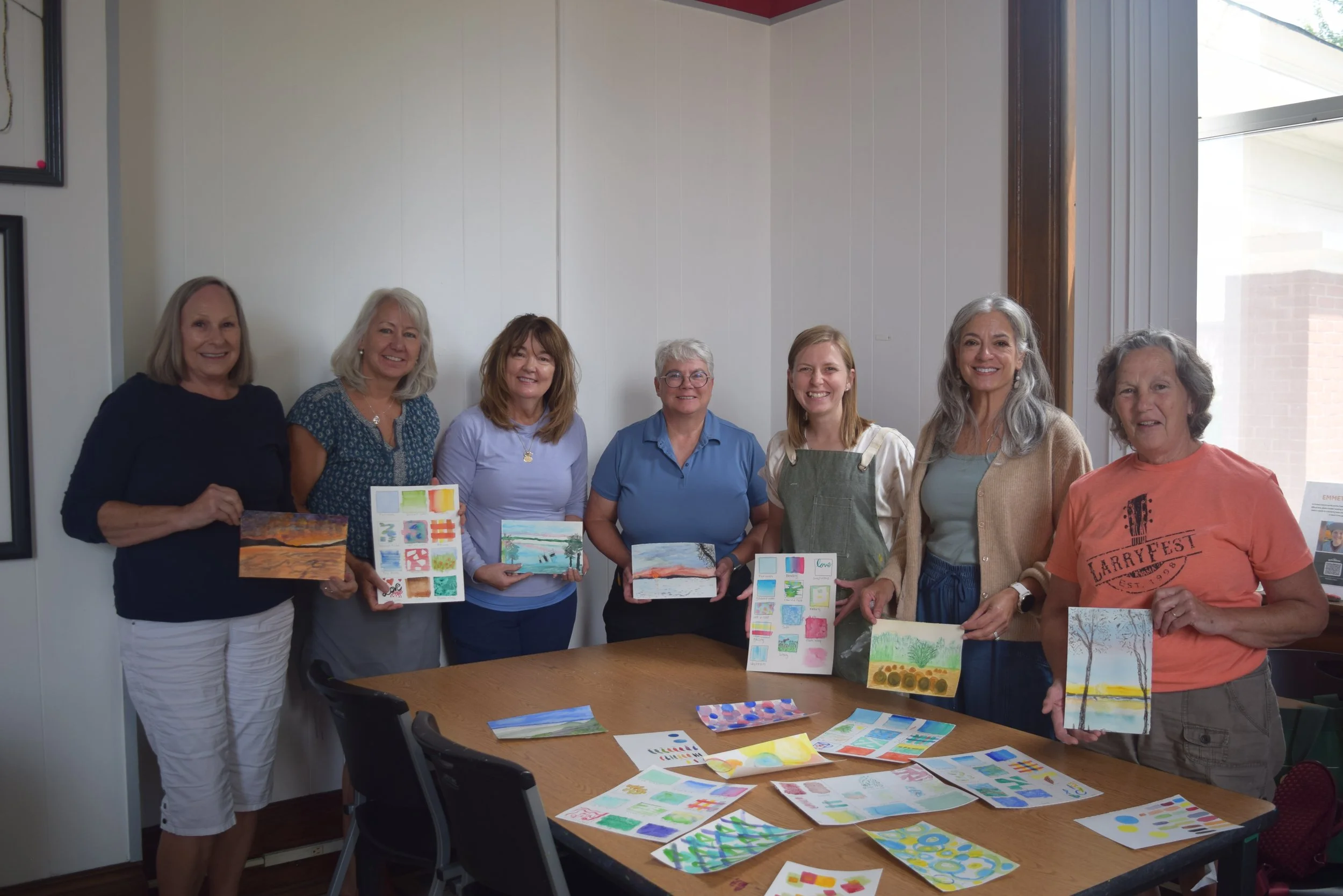 Group of adults display their finished watercolor and mixed-media artwork after a class in the Town Square MakerSpace.
