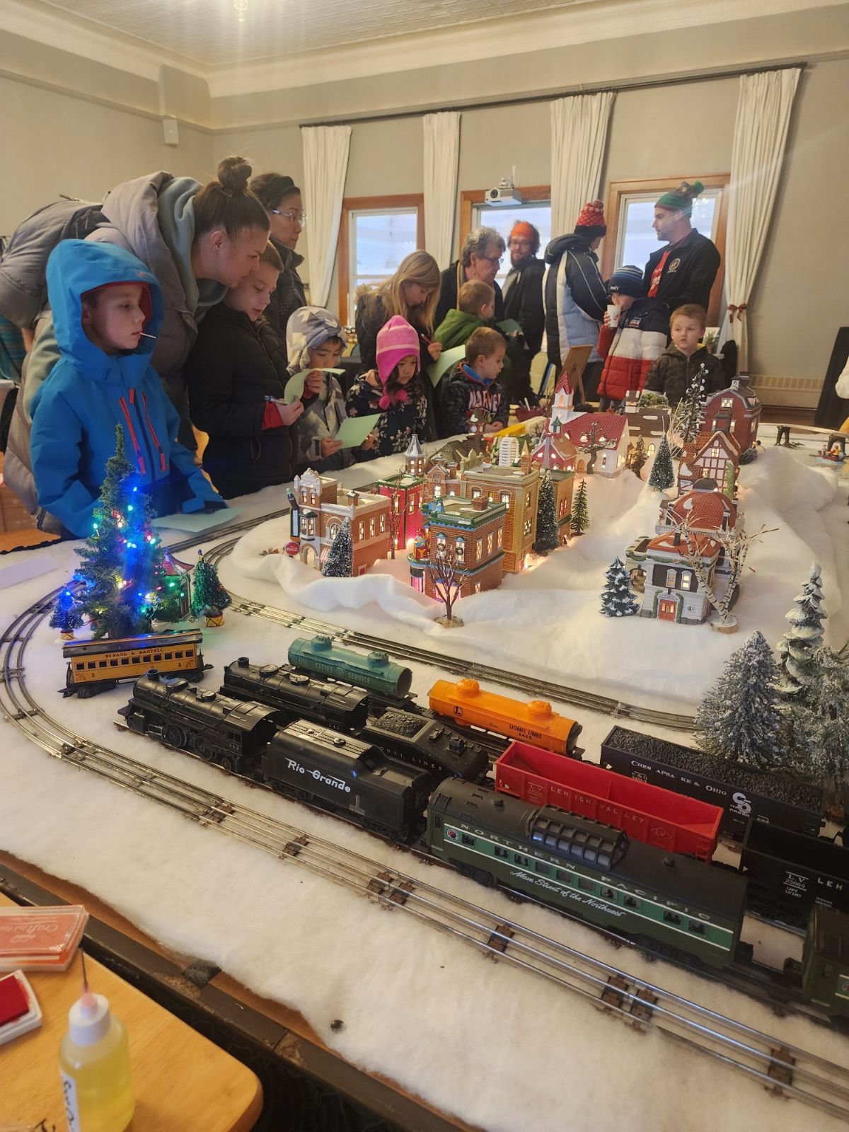 Families gather around a festive model train display with miniature buildings and snowy scenery at Town Square.