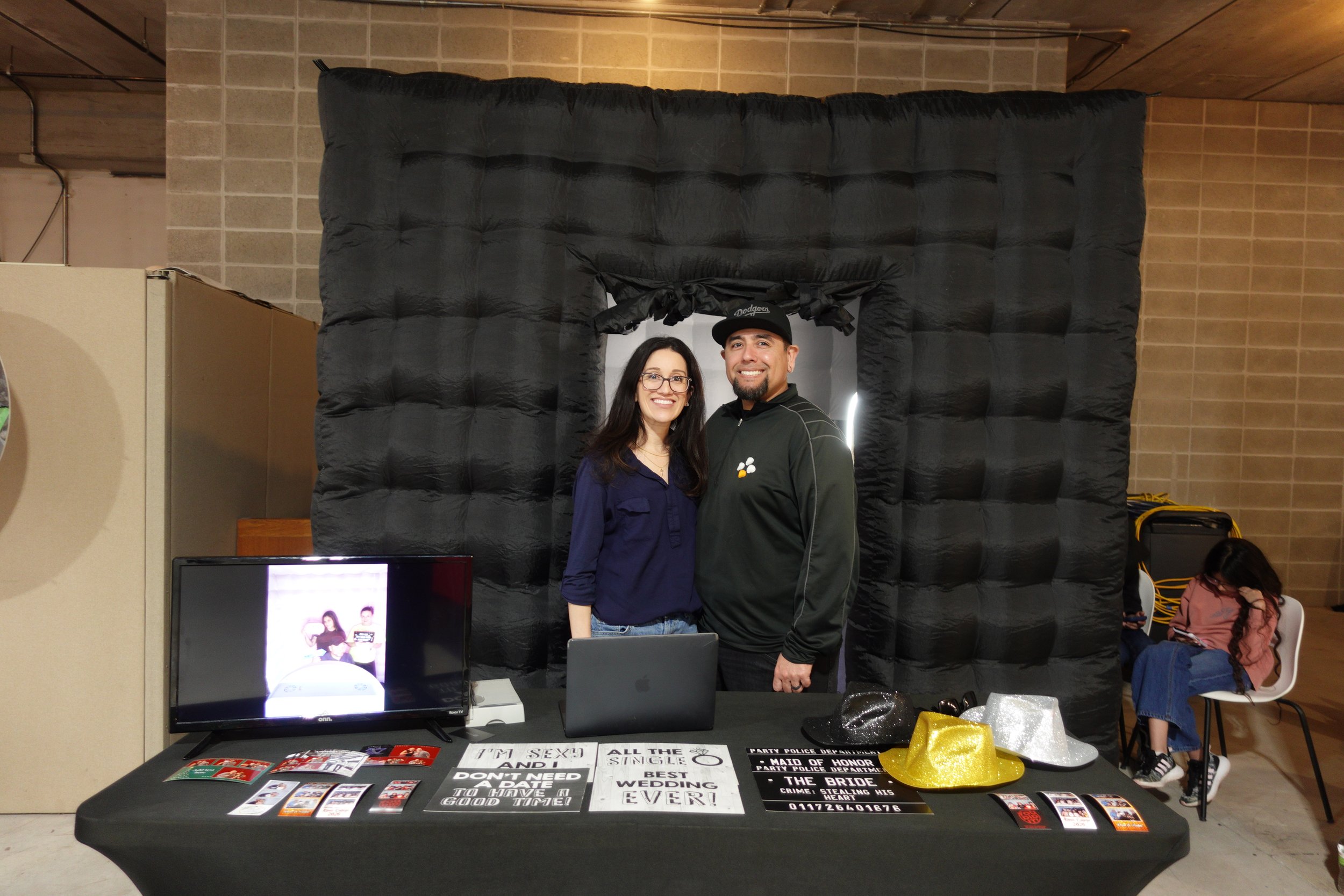 Two photo booth exhibitors stand behind a display of props, photo samples and promotional materials at the Wedding & Event Expo.