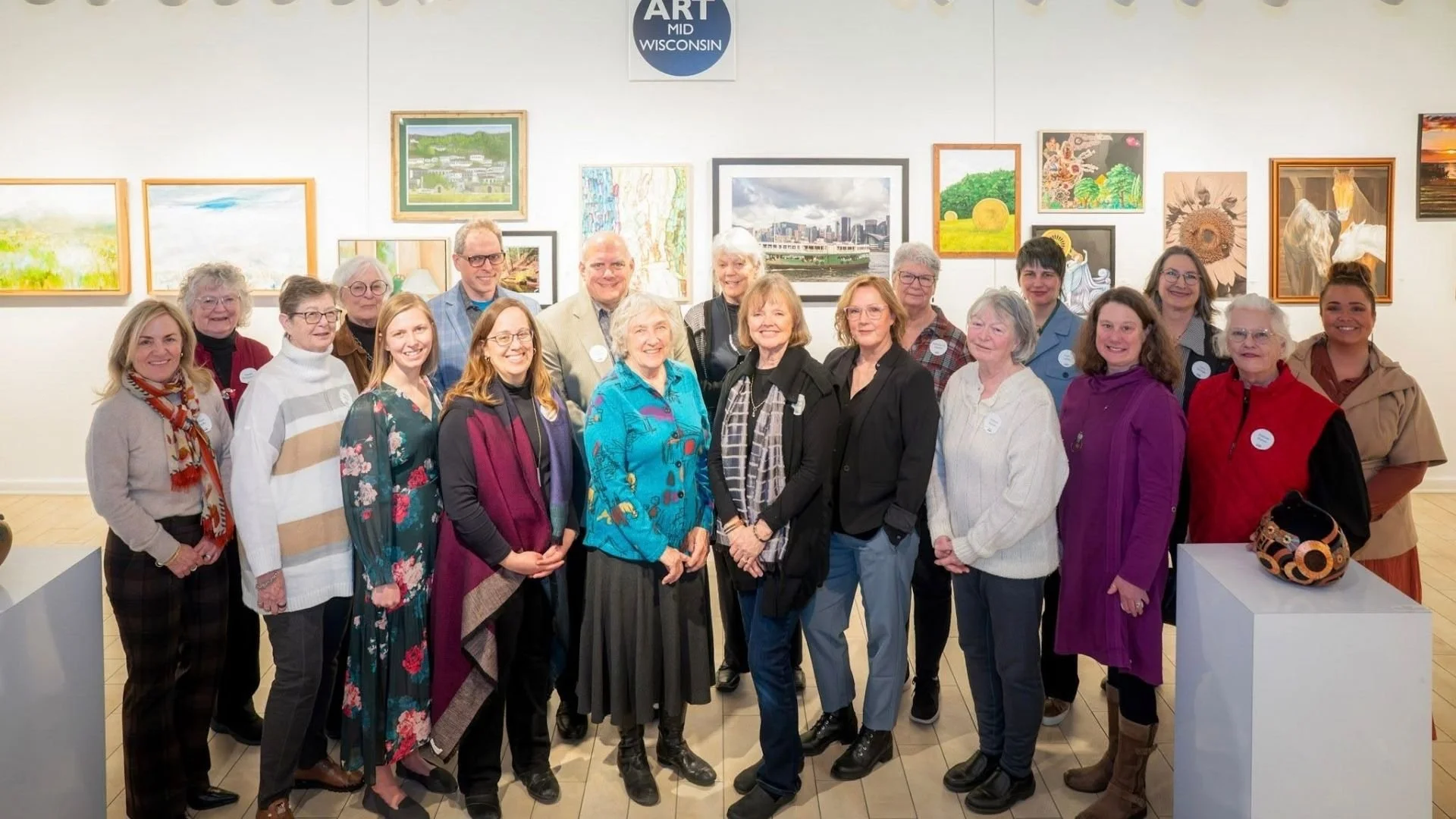 Art MidWisconsin artists gather for a group photo in a gallery surrounded by original artwork.