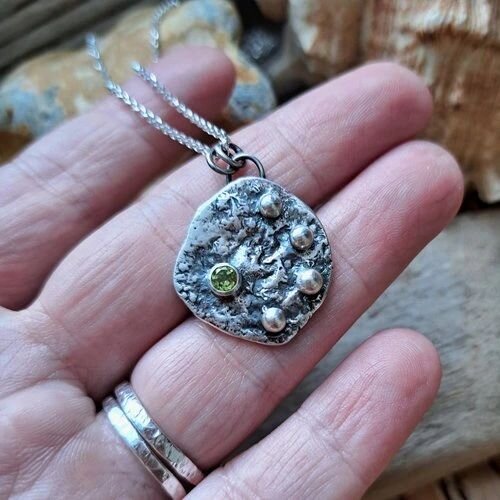 Rock pool peridot pendant in blackened sterling silver, which gives it that nibbly, nobbly, rocky, rustic look. This was made using reticulation, which essentially is the process of bringing all the fine silver to the surface to make one of a kind ri